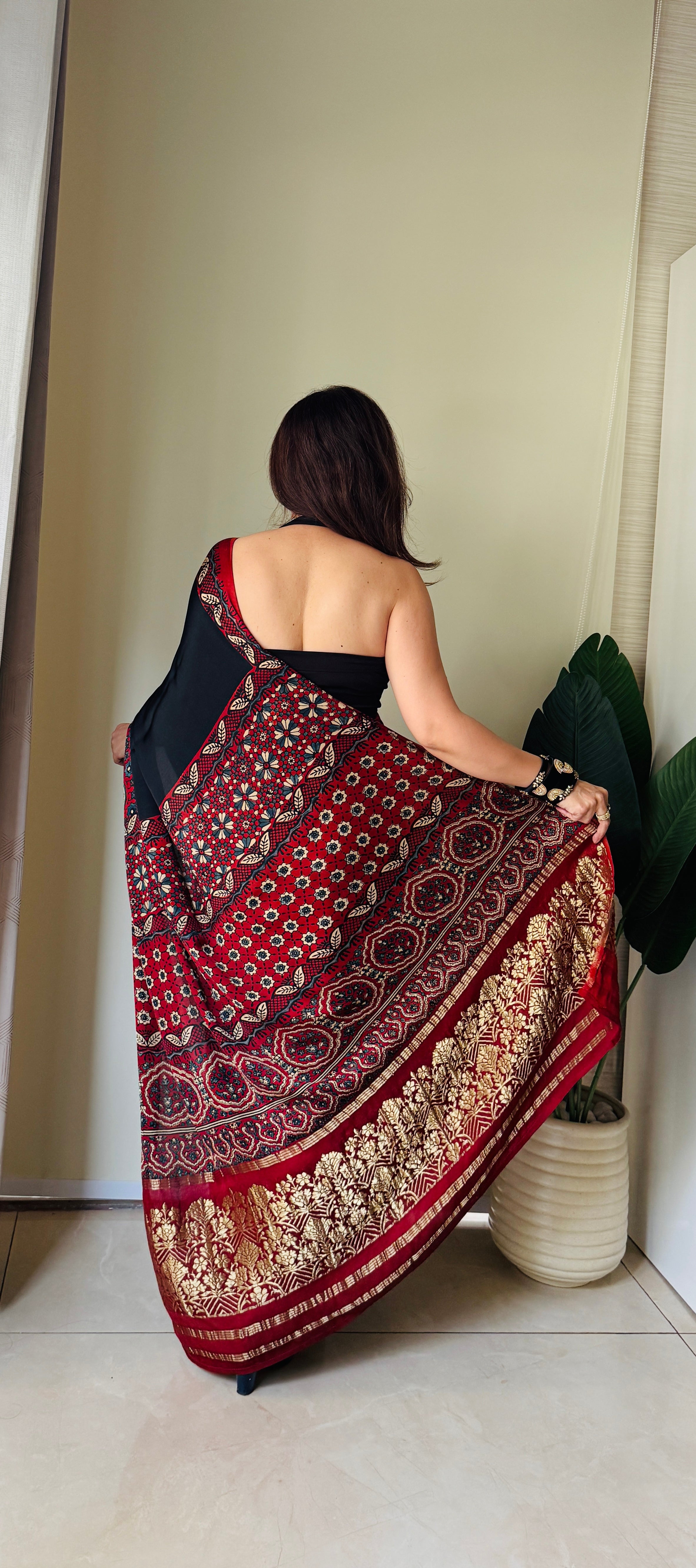 Woman wearing a red and black ajrakh saree with intricate traditional patterns and gold border