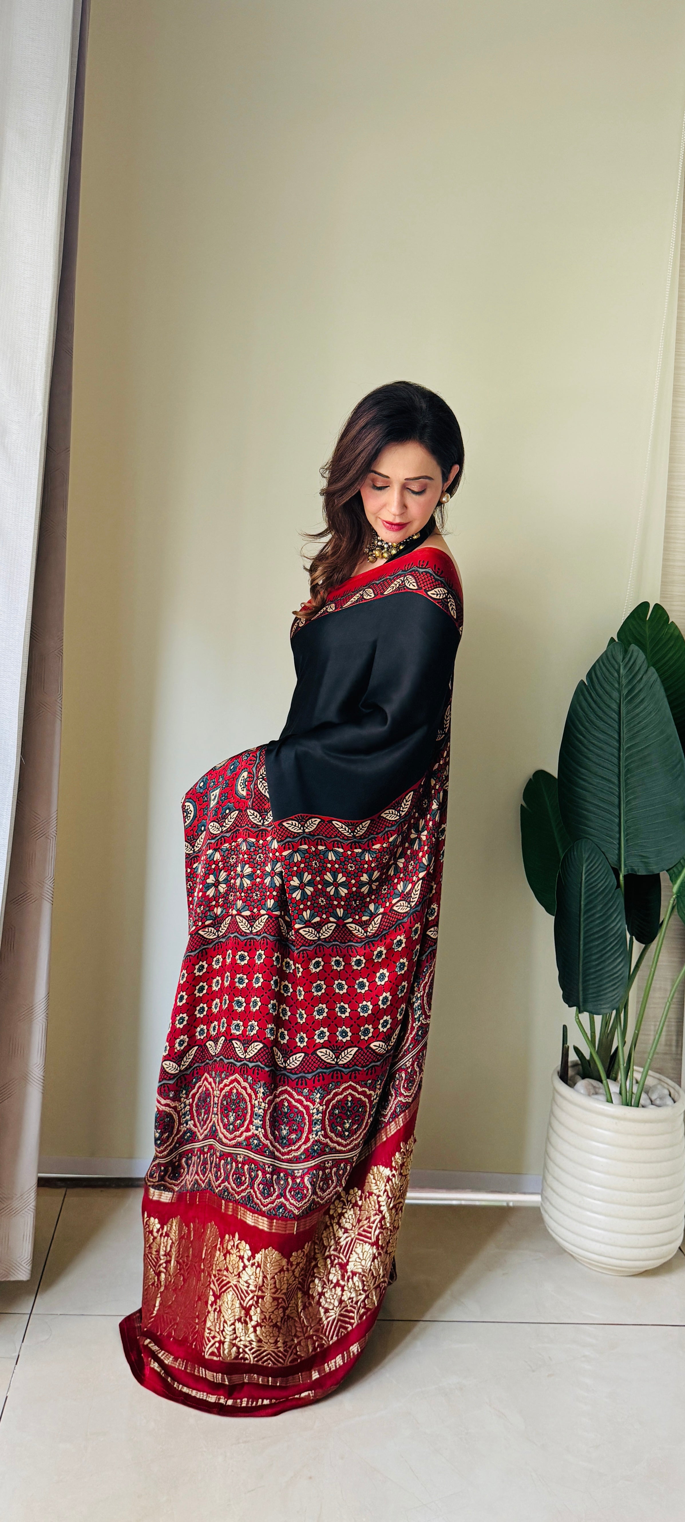 Kawaii ajrakh saree in red black with traditional patterns and gold border worn by woman indoors