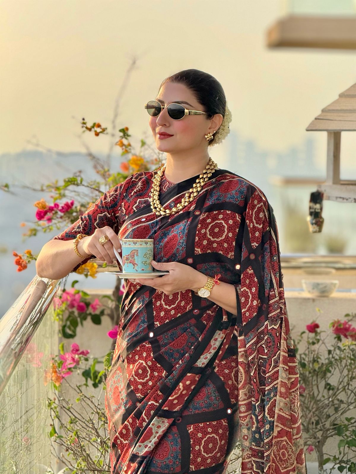 Kawaii ajrakh saree with floral and geometric patterns worn by woman holding a cup outdoors