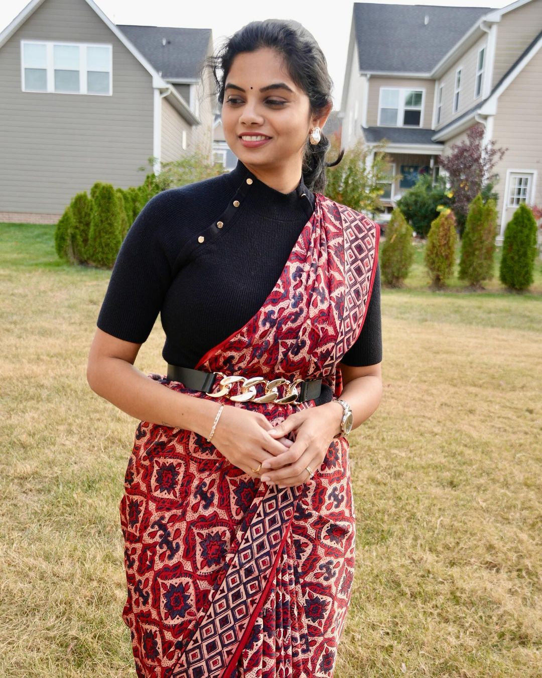 Woman wearing a red and black patterned ajrakh saree with a black blouse and gold belt outdoors