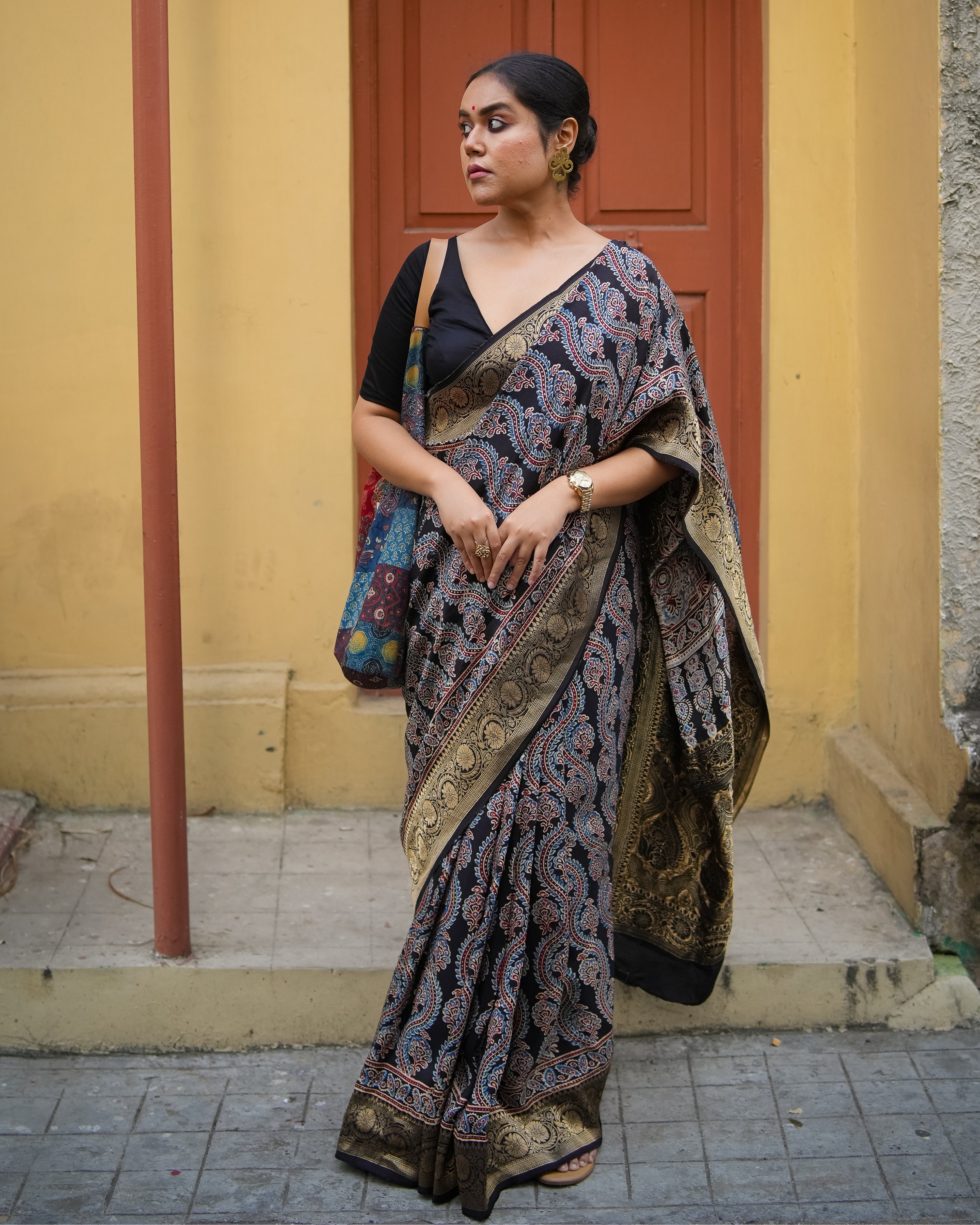 Woman wearing a black and gold ajrakh saree with intricate patterns standing outdoors