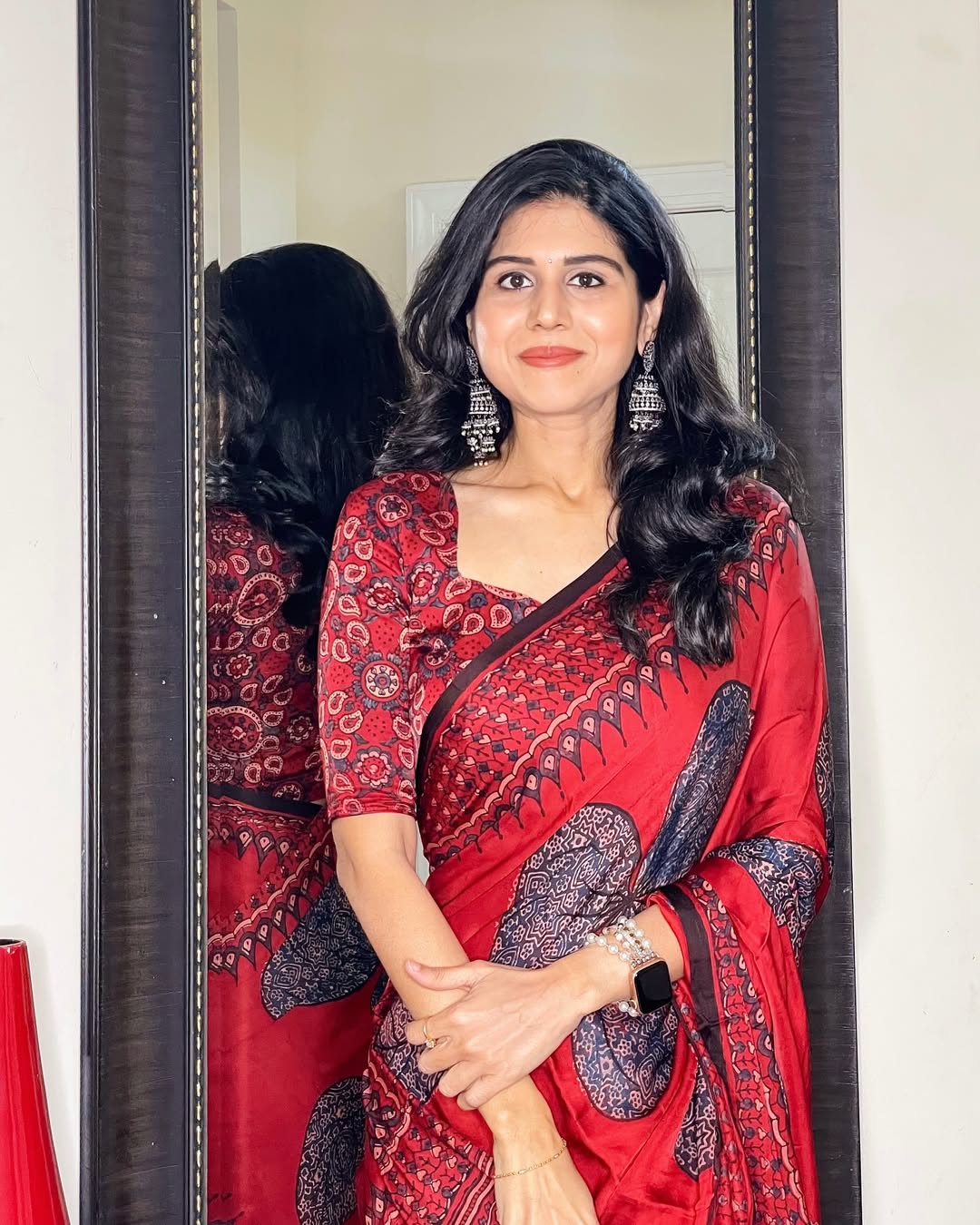 Woman wearing a red ajrakh saree with detailed traditional prints standing in front of a mirror