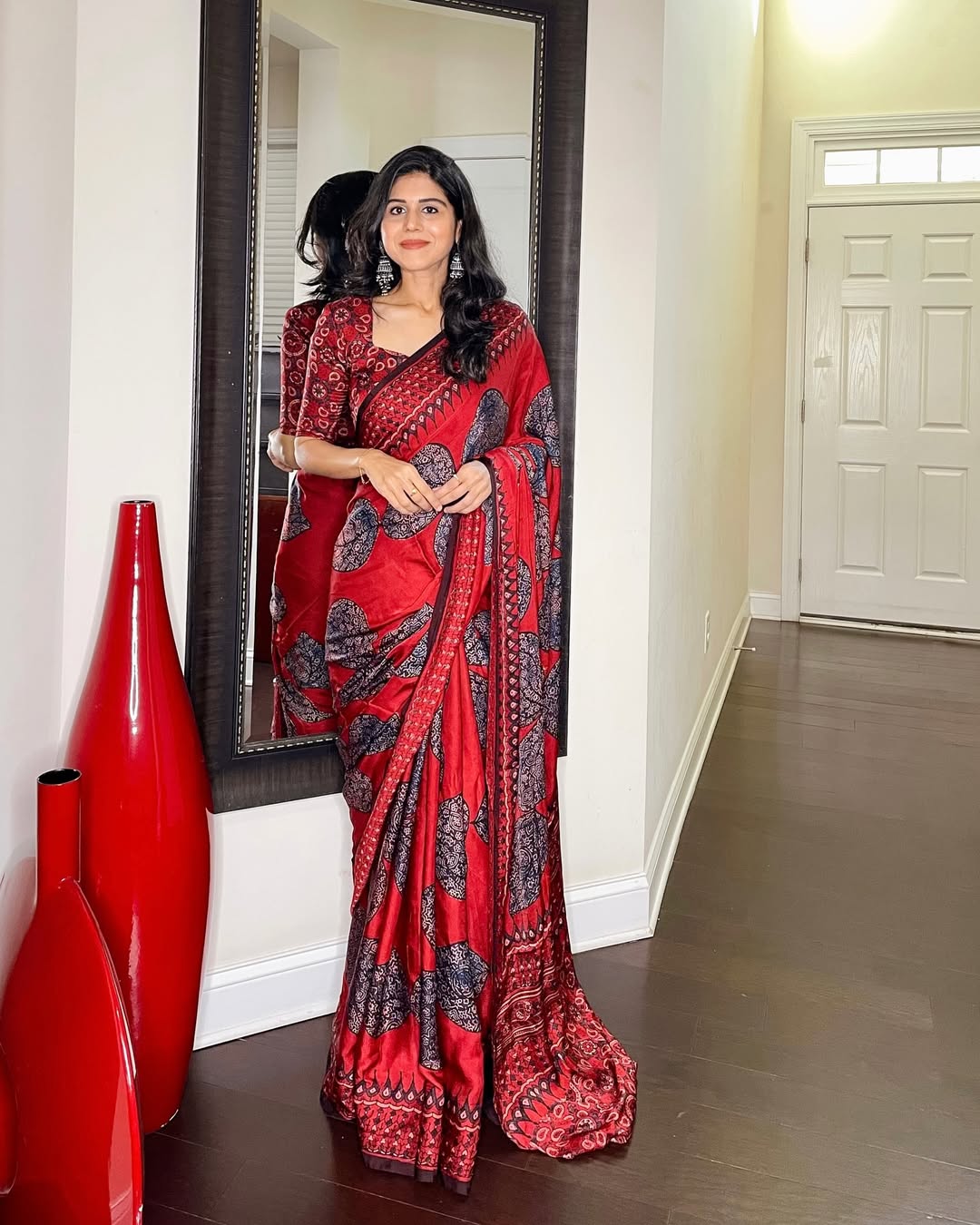 Woman wearing a red and black patterned ajrakh saree standing beside a mirror indoors
