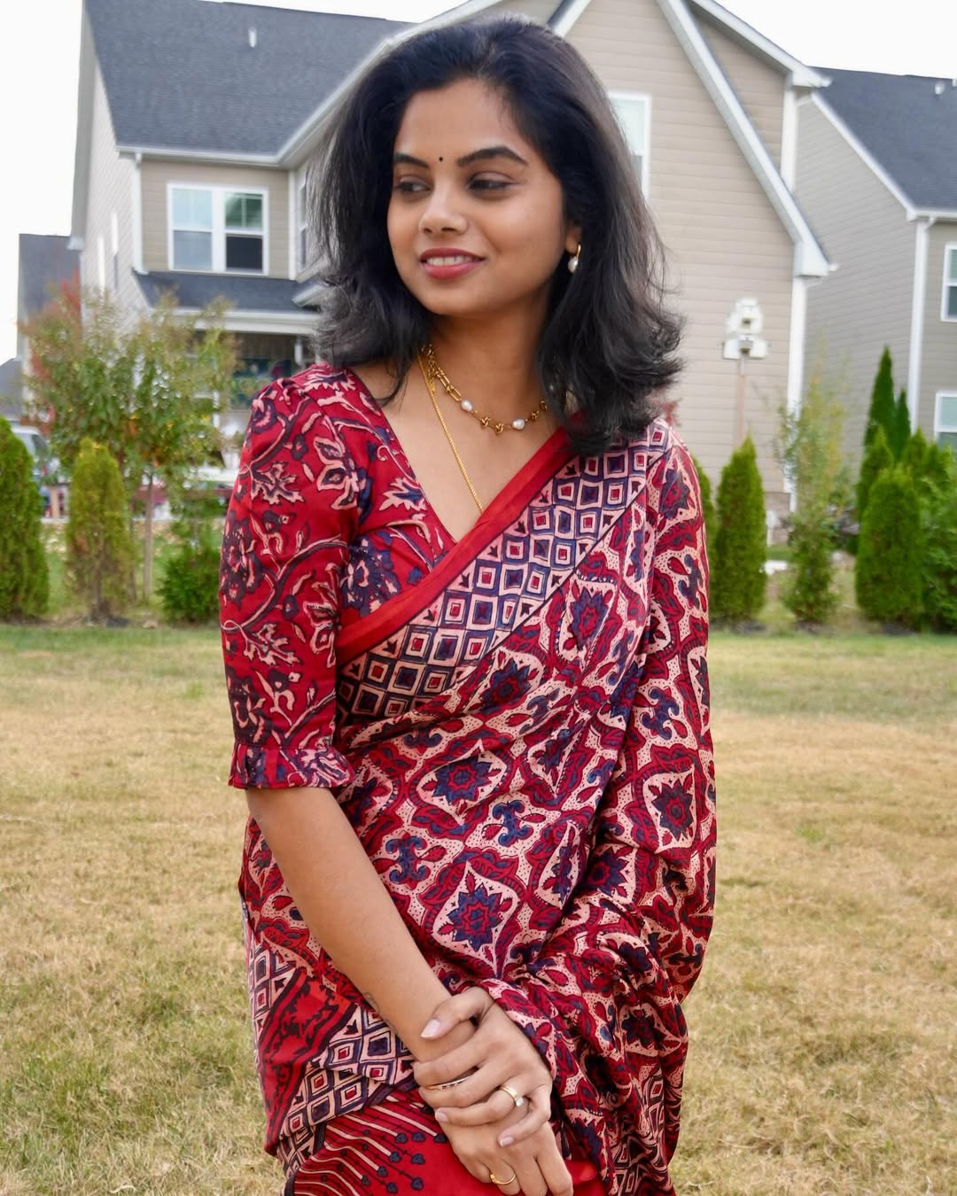Woman wearing a red and blue patterned ajrakh saree by Kawaii standing outdoors near houses