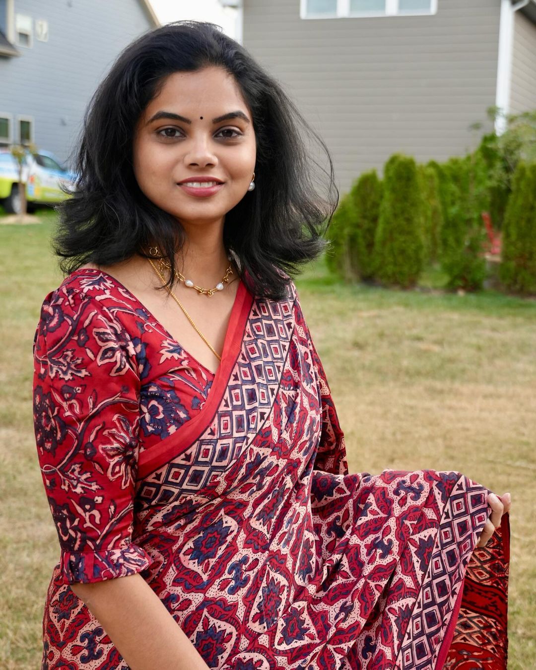 Woman wearing a red and blue patterned ajrakh saree by Kawaii sitting outdoors with greenery in the background