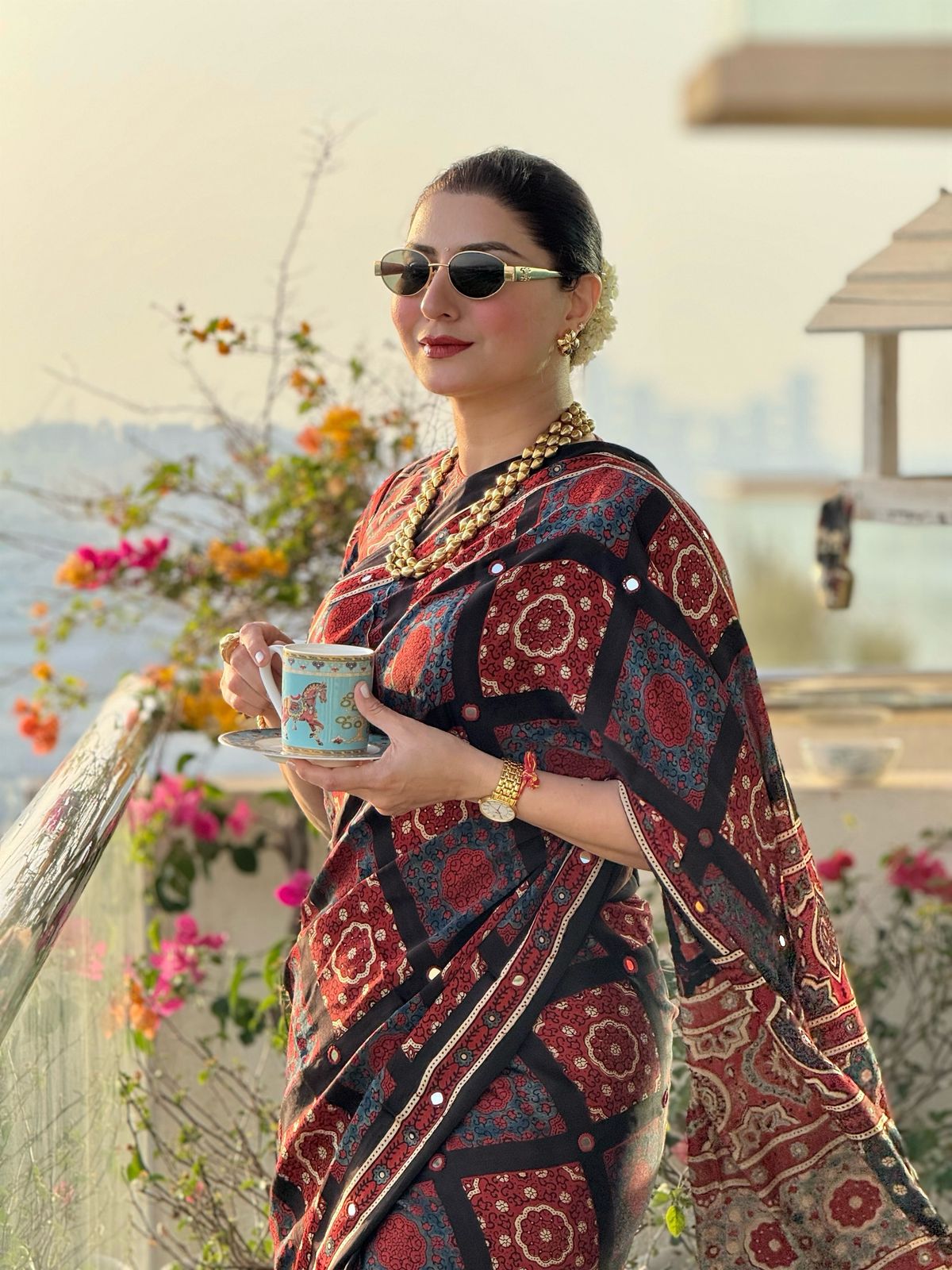 Woman wearing Kawaii floral ajrakh saree with sunglasses holding a teacup outdoors
