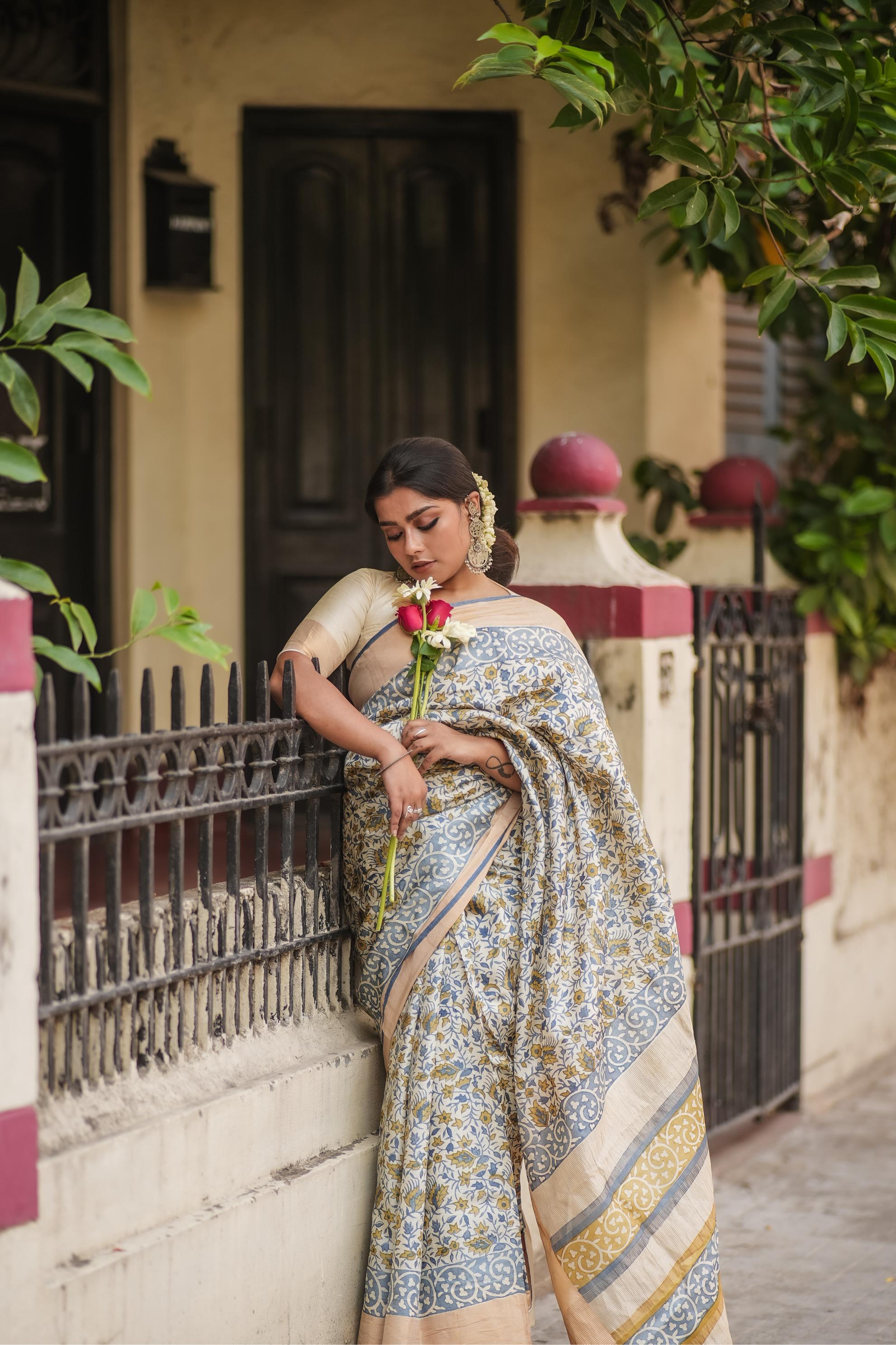 Woman wearing Kawaii block print saree with floral patterns holding a rose near a railing outdoors