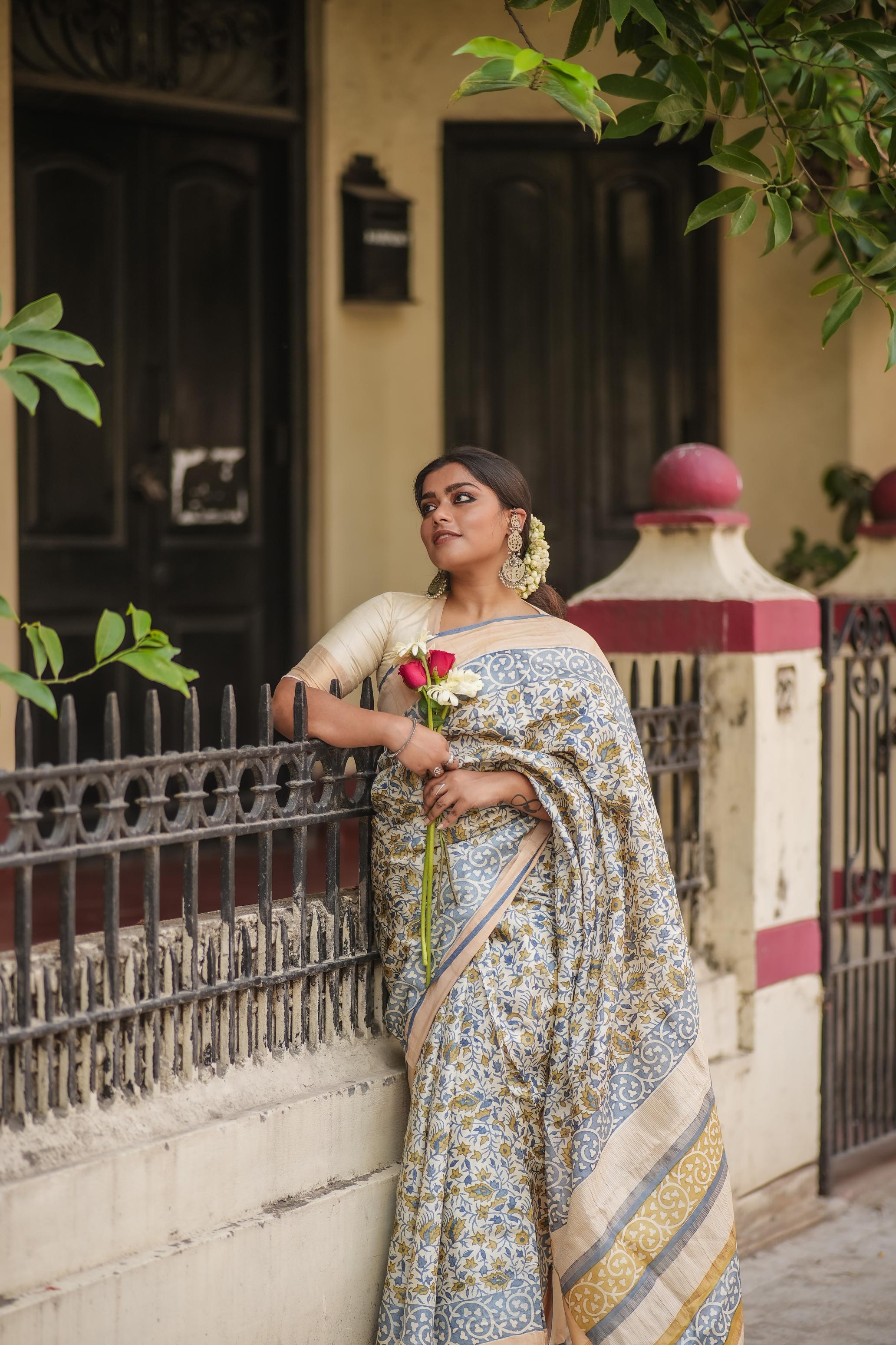 Woman wearing Kawaii block print saree holding a red rose standing by wrought iron fence