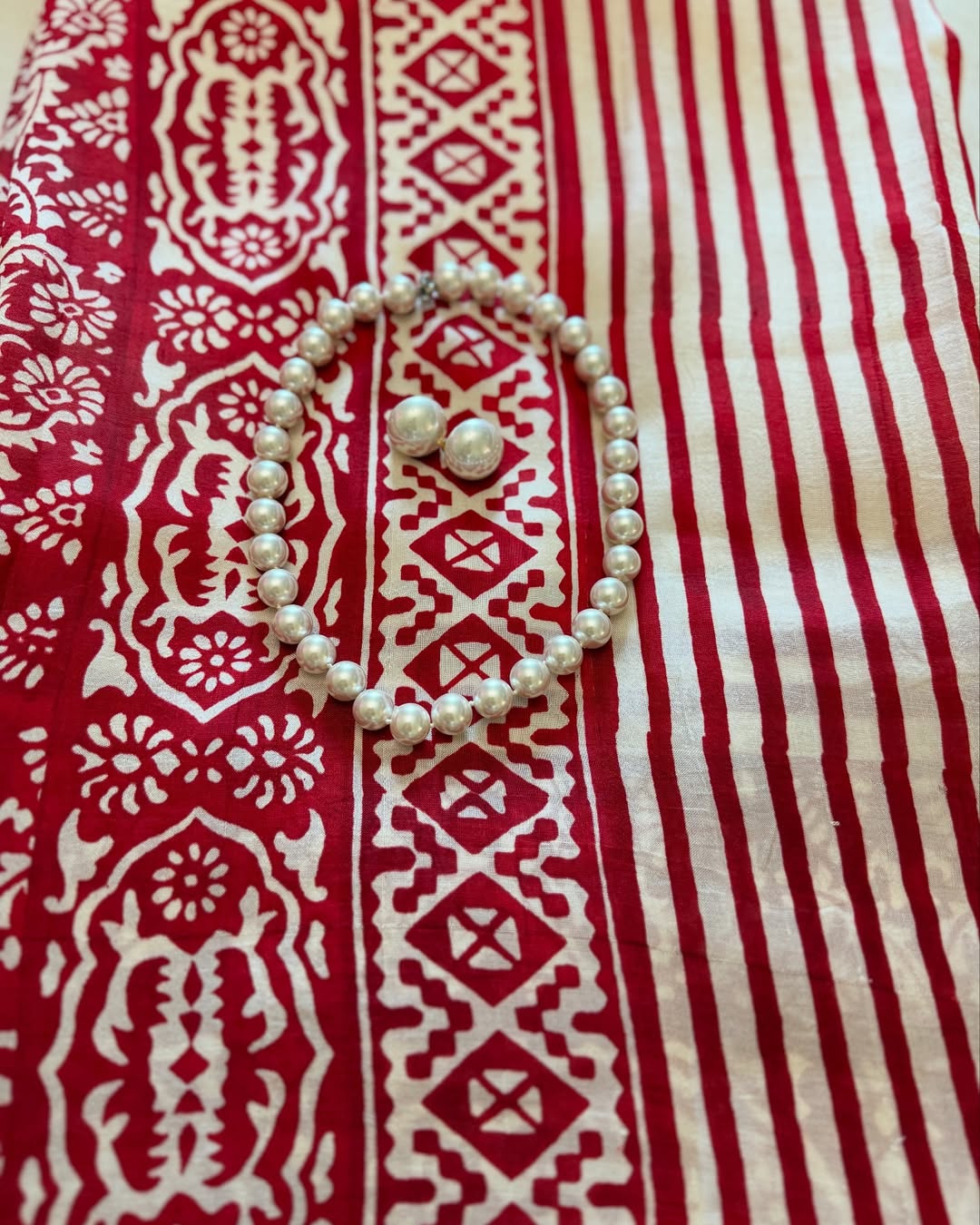 Kawaii block print saree in red and white featuring intricate designs and paired with a pearl necklace and earrings