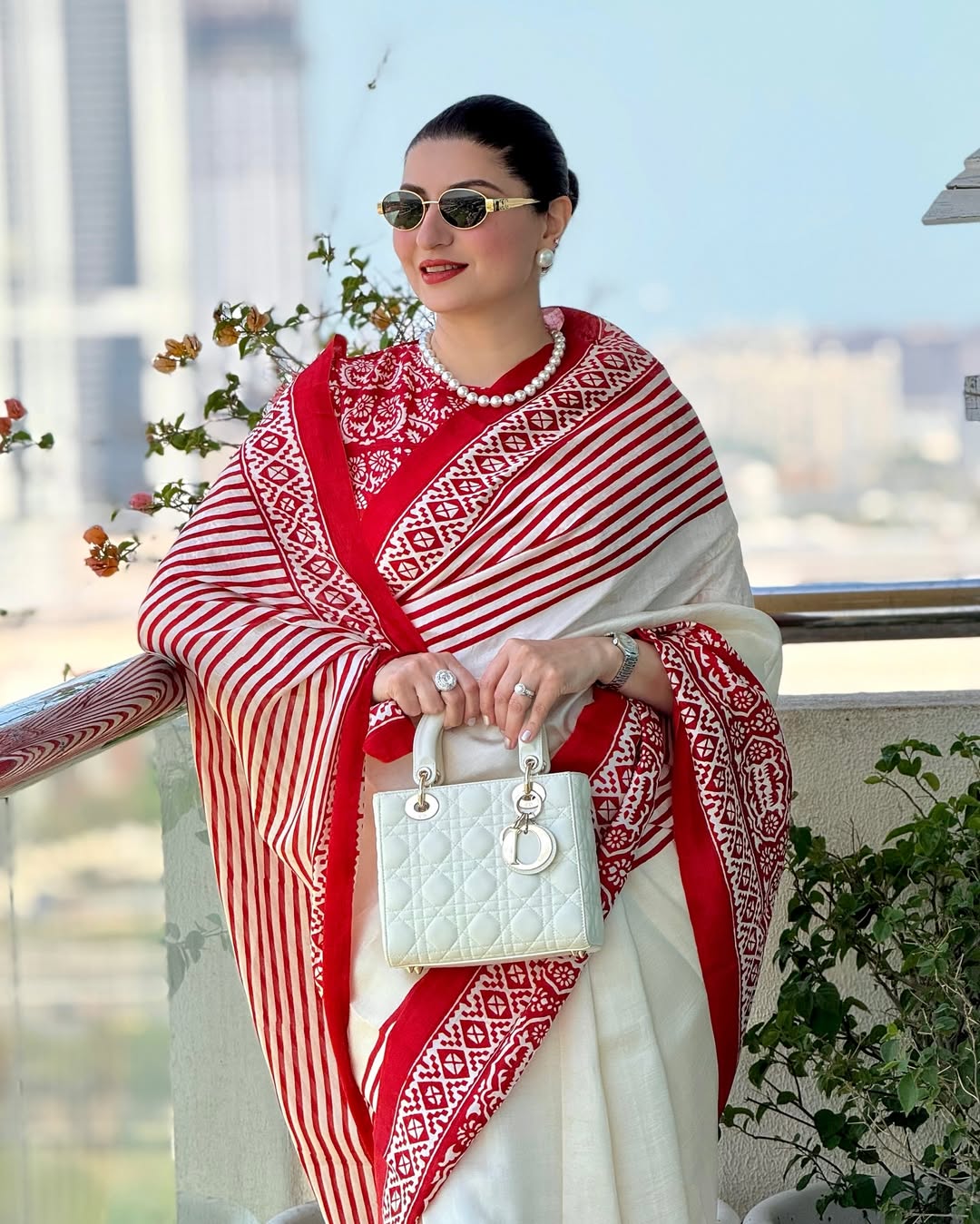 Woman wearing red and white block print saree by Kawaii with pearl necklace and white handbag