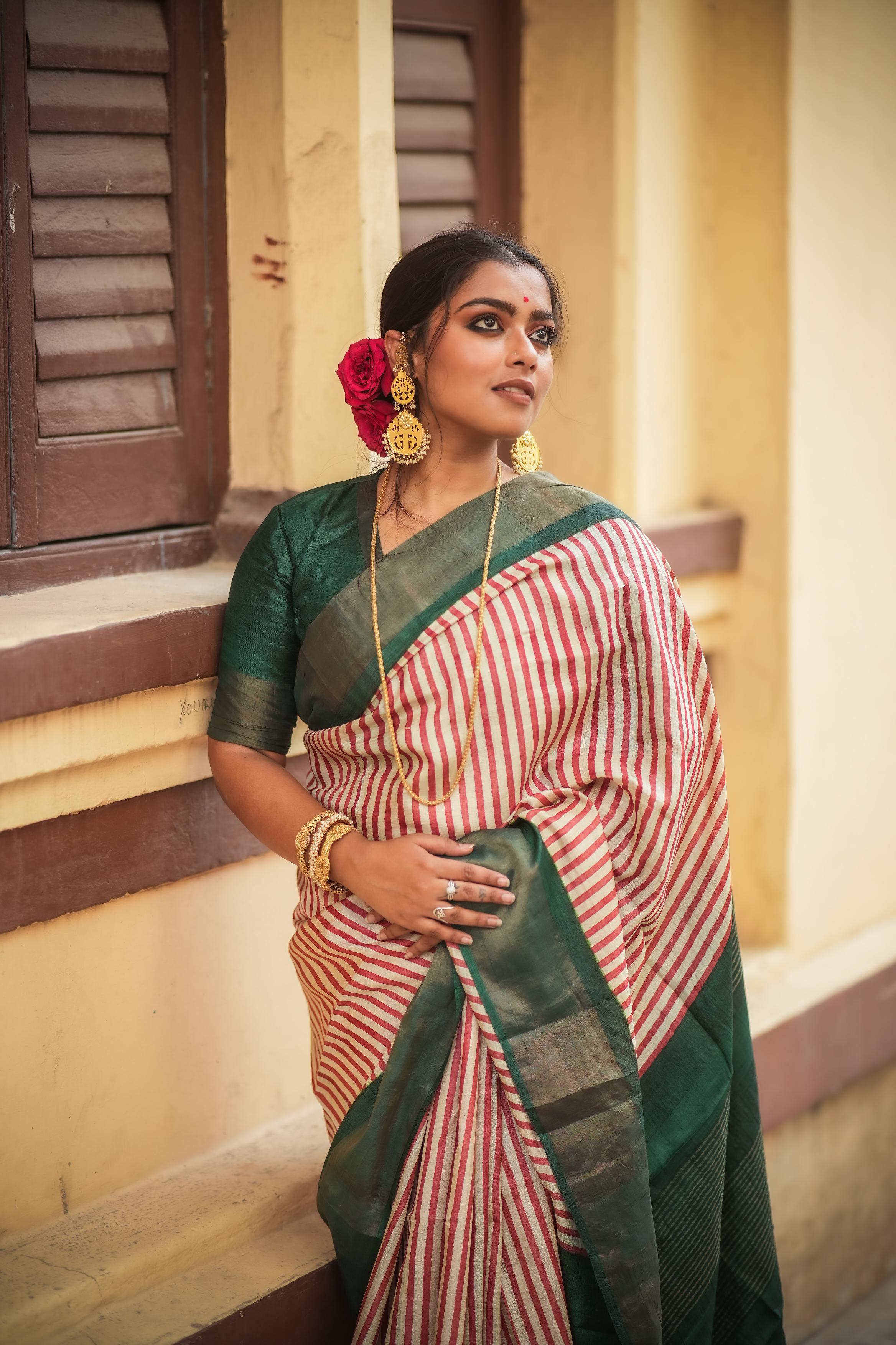 Woman wearing a striped green and cream block print saree with gold jewelry and floral hair accessories