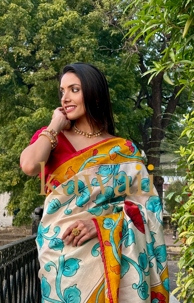 Elegant kalamkari saree featuring blue and red floral designs on soft cream fabric, worn with a red blouse