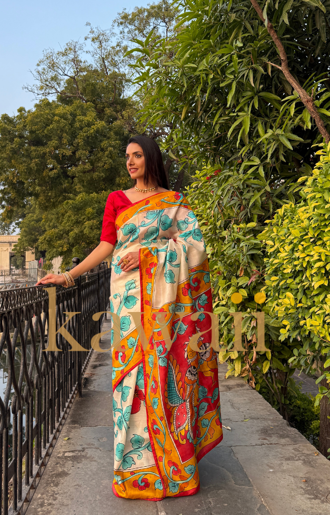 Elegant kalamkari saree in cream with vibrant blue and red floral patterns, perfect for festive occasions.