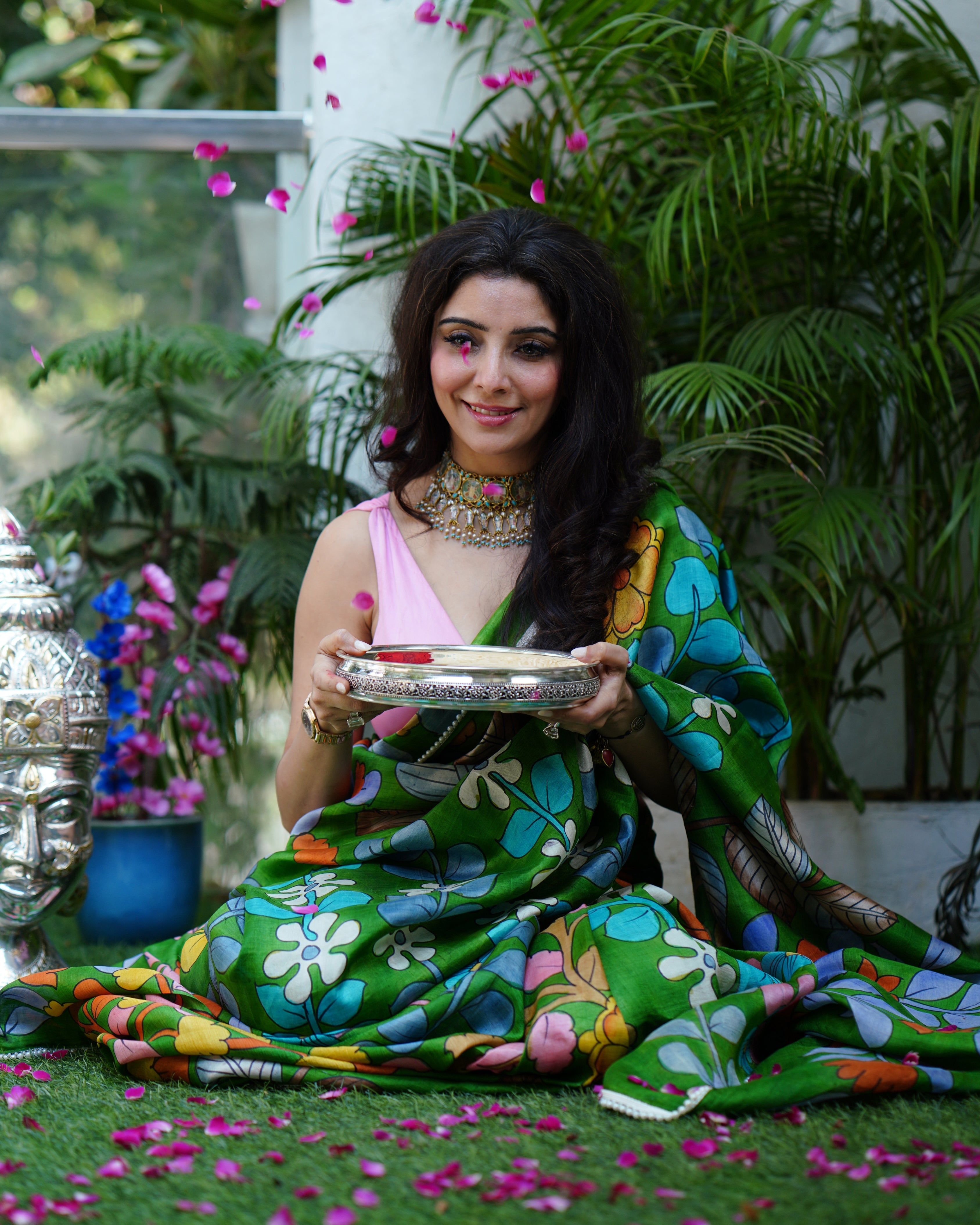 Woman wearing colorful green Kawaii kalamkari saree with floral patterns sitting outdoors holding a decorative plate