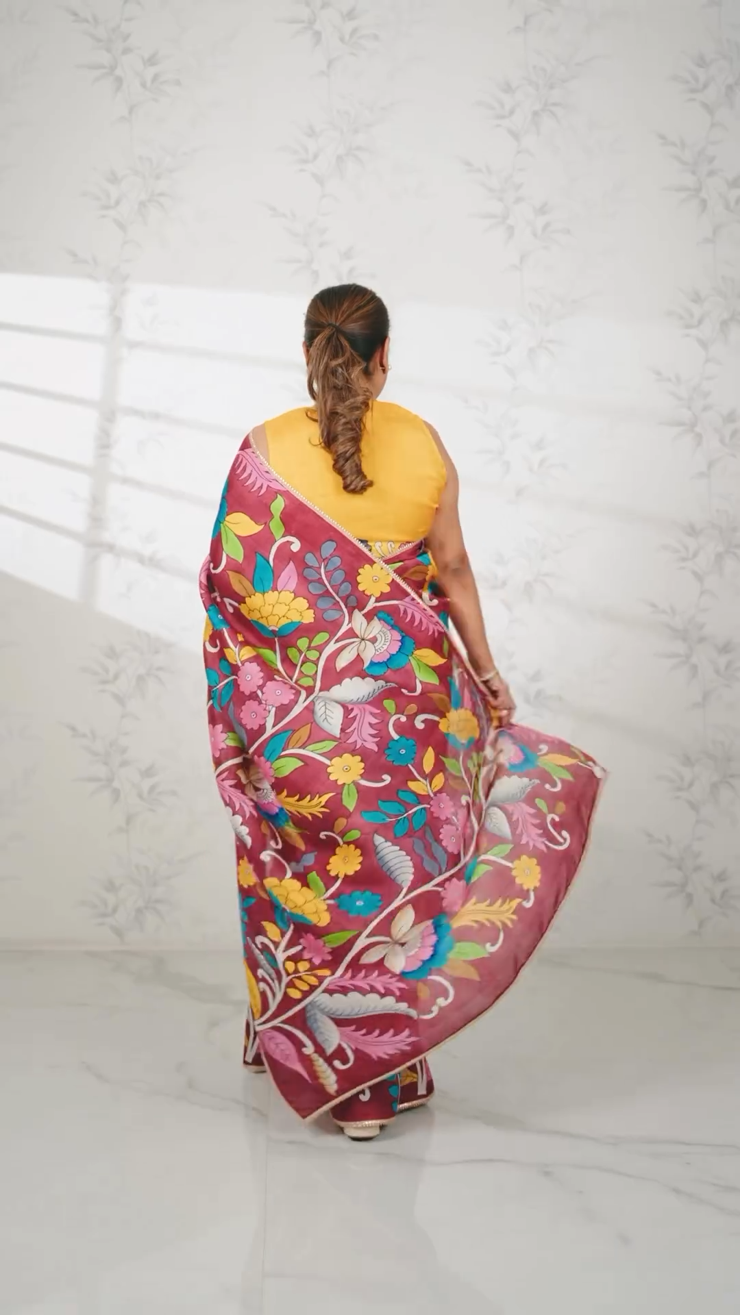 Woman wearing colorful Kawaii kalamkari saree with floral patterns and yellow blouse, shown from back