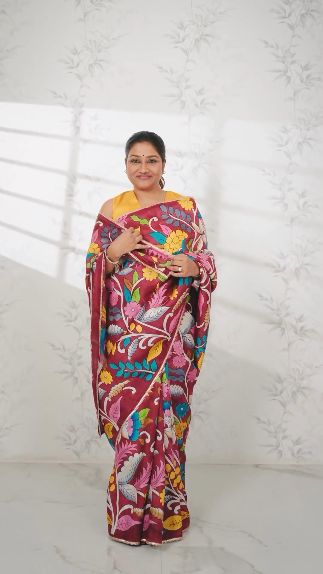 Kawaii kalamkari saree in maroon with vibrant floral patterns worn by a smiling woman