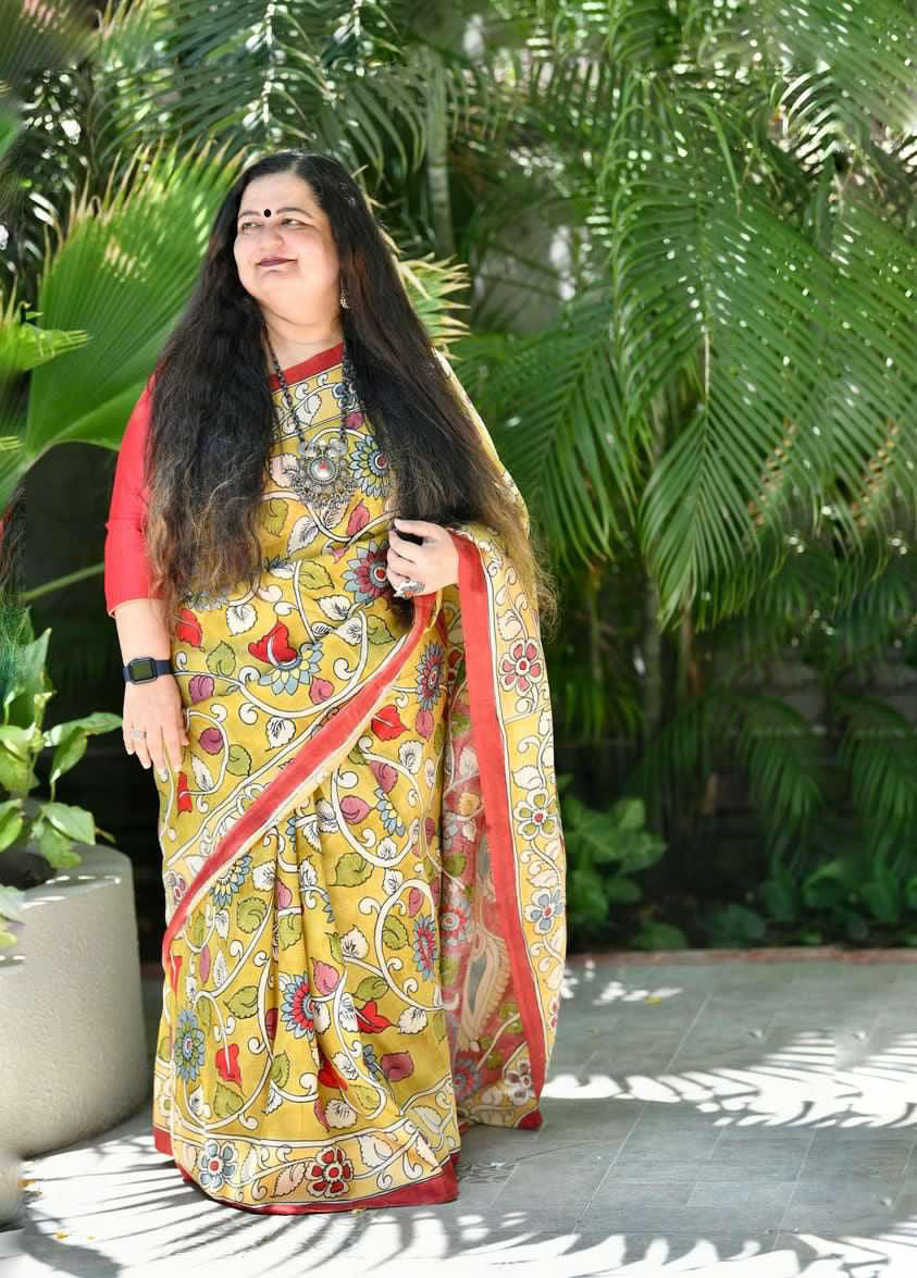Kawaii yellow and red kalamkari saree with floral patterns worn by woman in outdoor garden