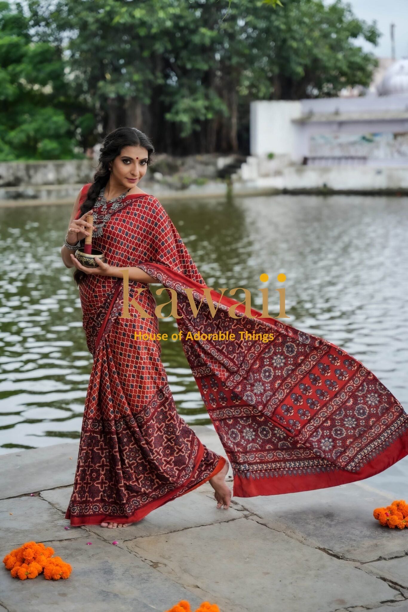 Woman wearing a red and black patterned ajrakh saree by Kawaii standing near water with floral decorations