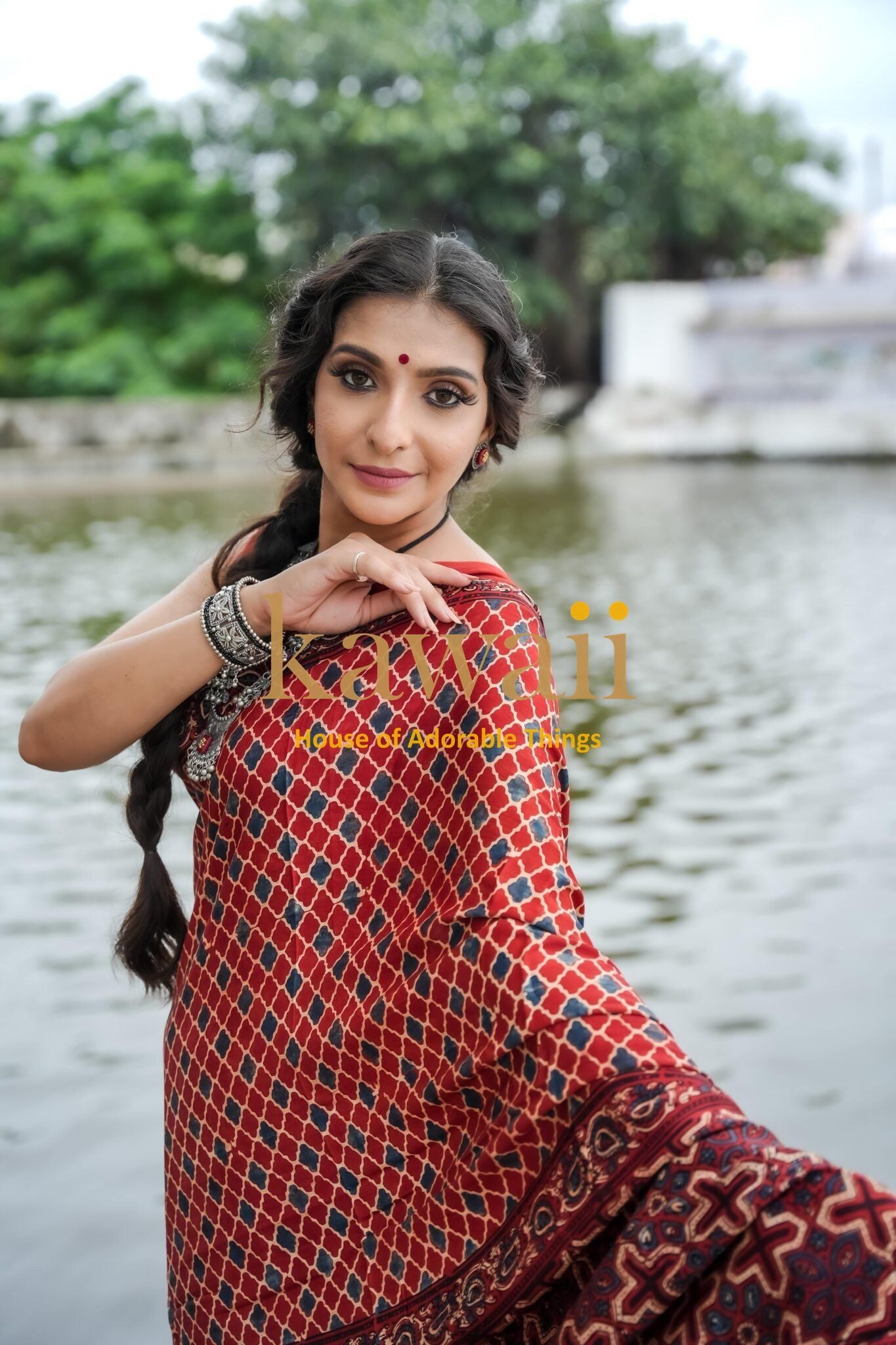 Woman wearing a red patterned ajrakh saree by Kawaii standing near water with braided hair