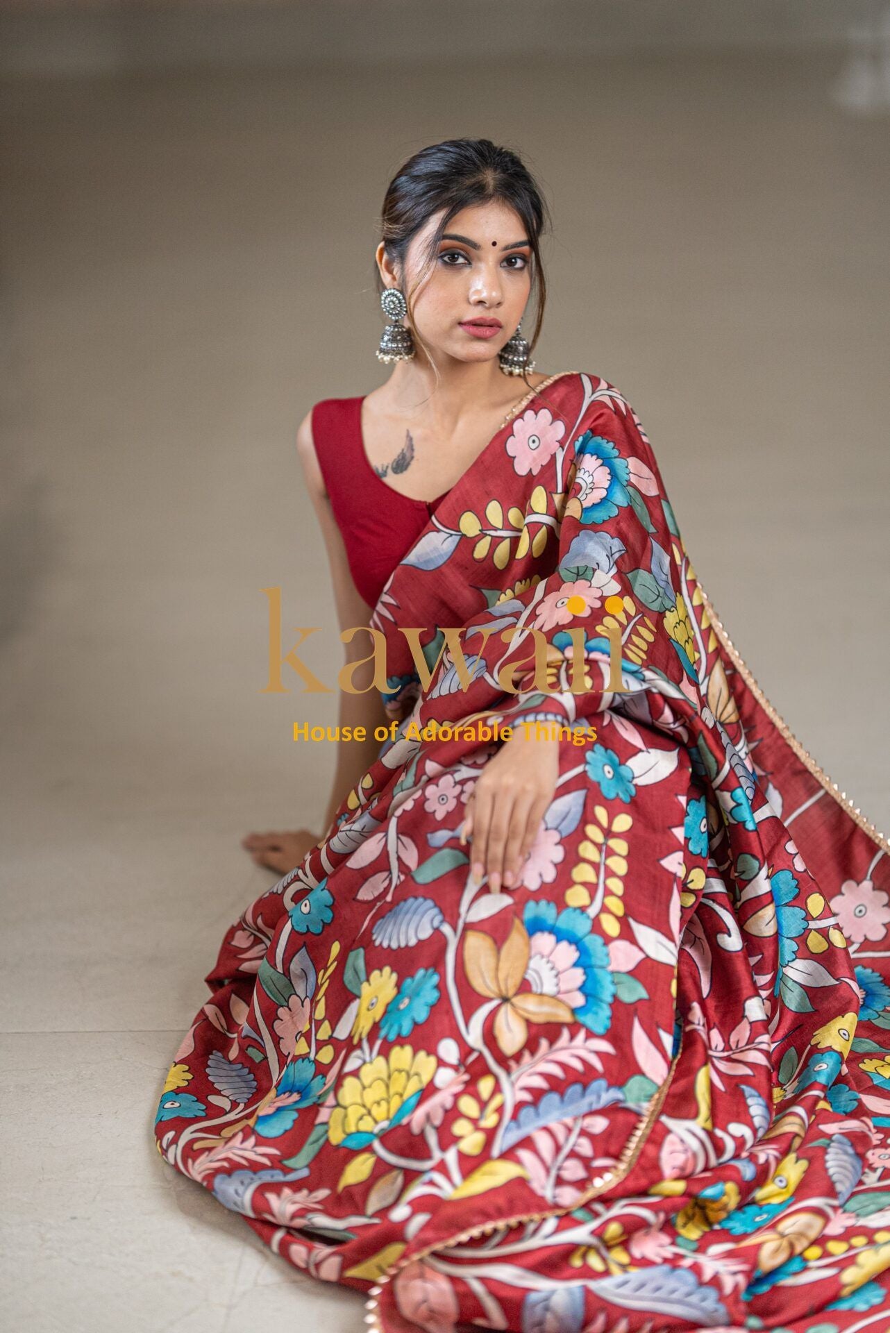 Woman wearing a vibrant red kalamkari saree with colorful floral patterns and traditional jewelry