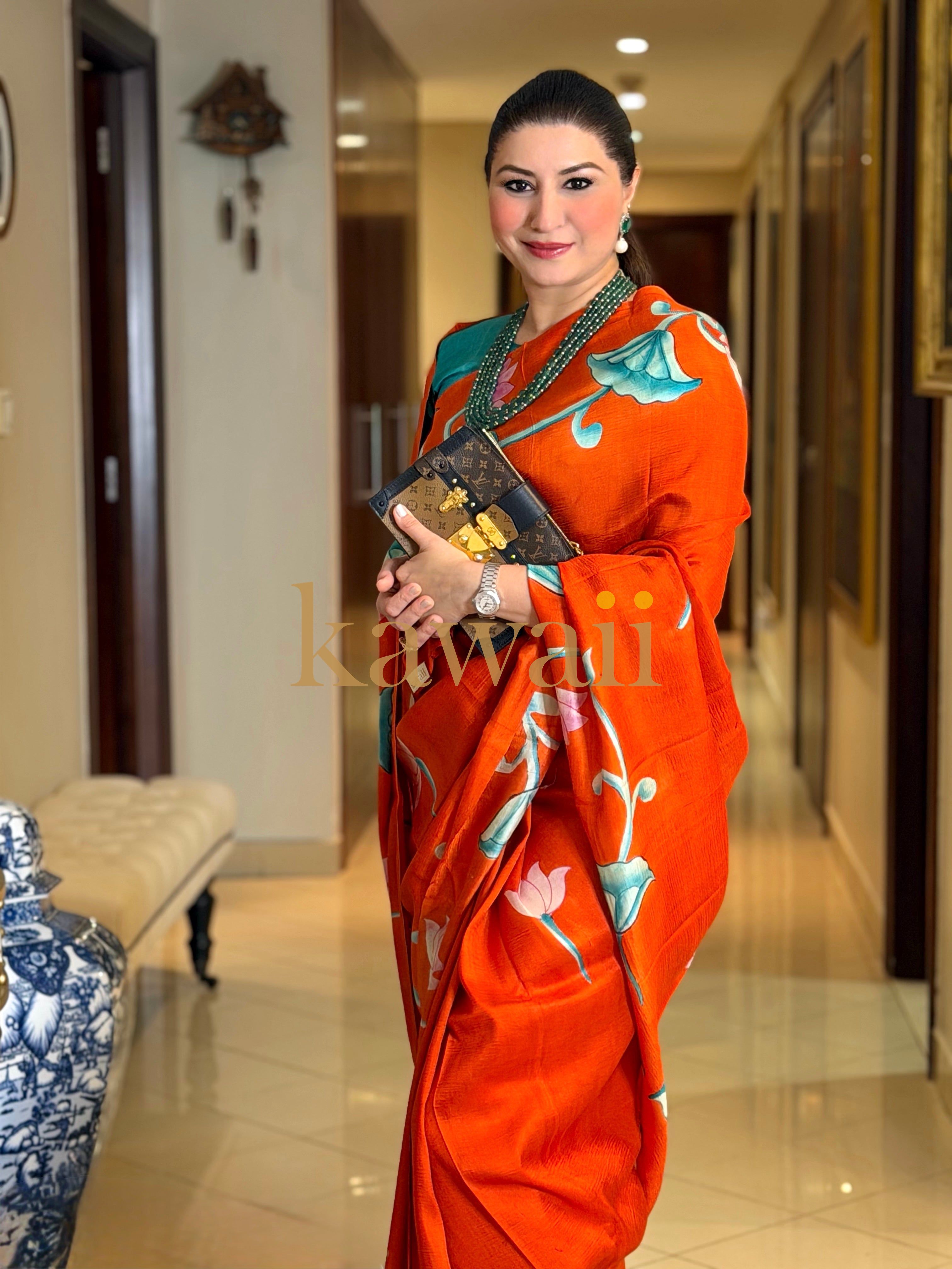 Elegant woman wearing a vibrant orange pichwai saree with floral designs, styled for a formal setting
