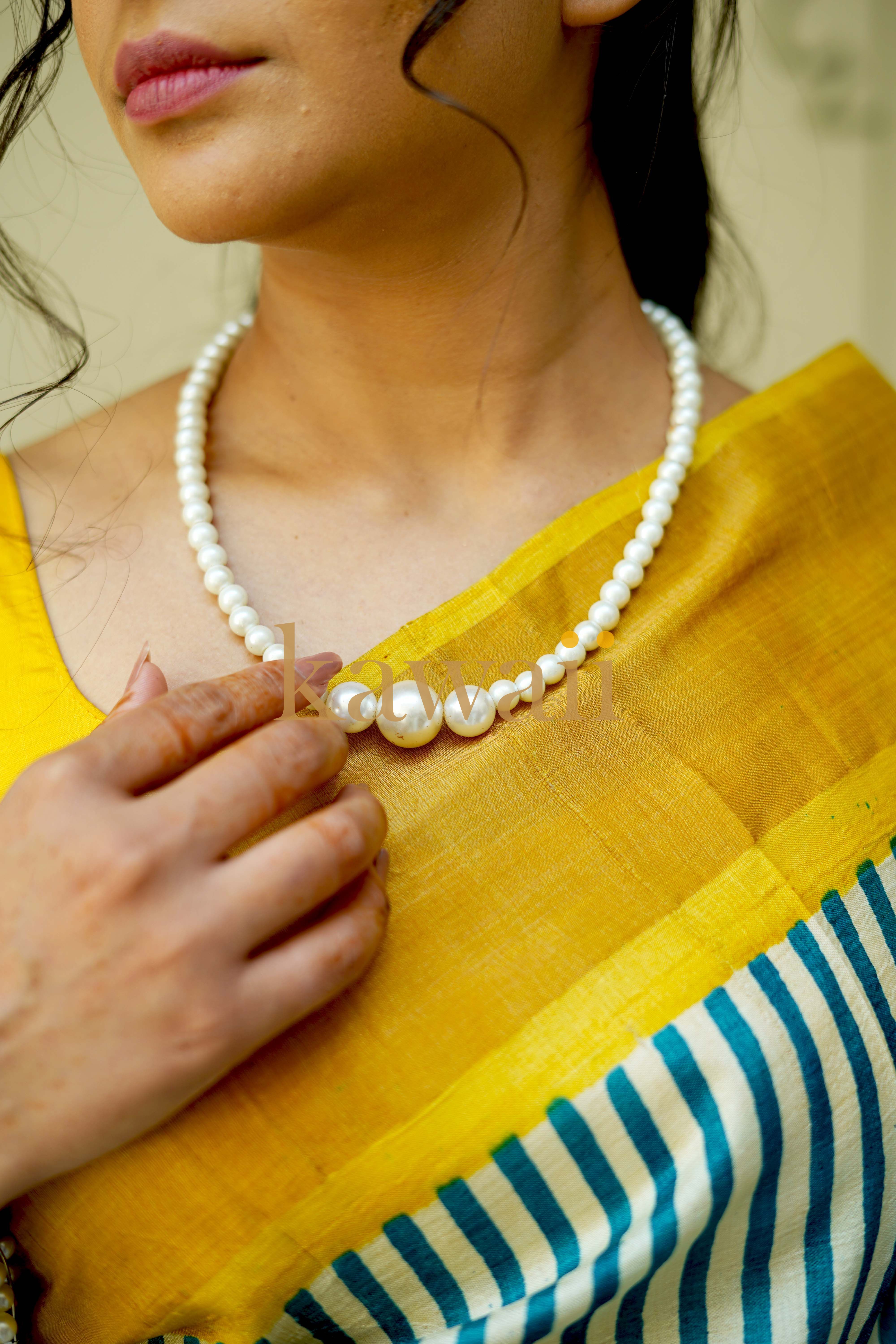 Model wearing a yellow block print tussar silk saree with blue stripes and pearl necklace