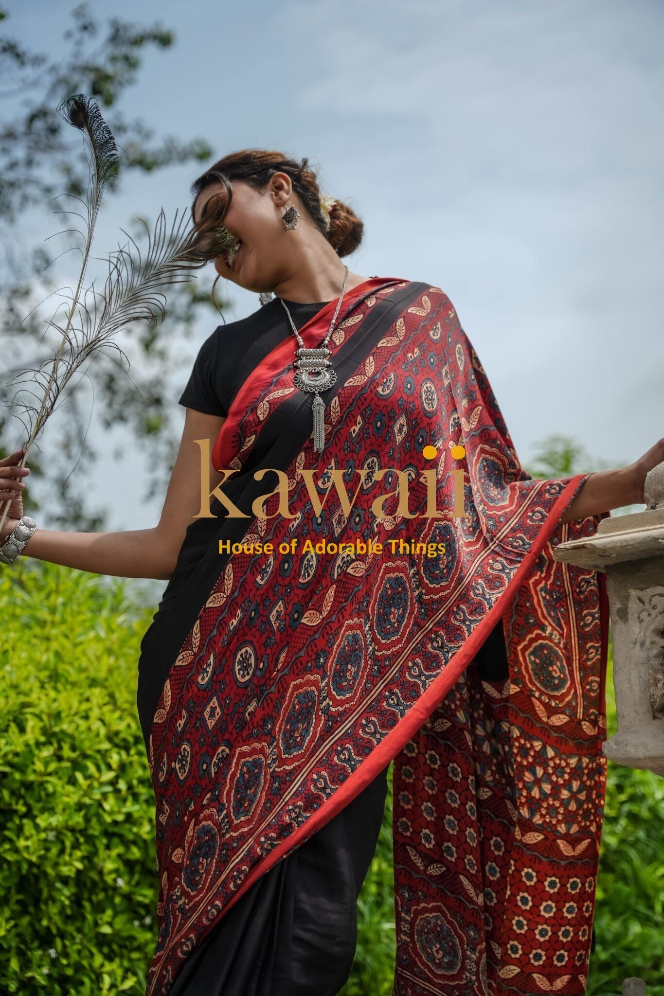Woman wearing a red and black ajrakh saree with traditional patterns outdoors by a stone railing