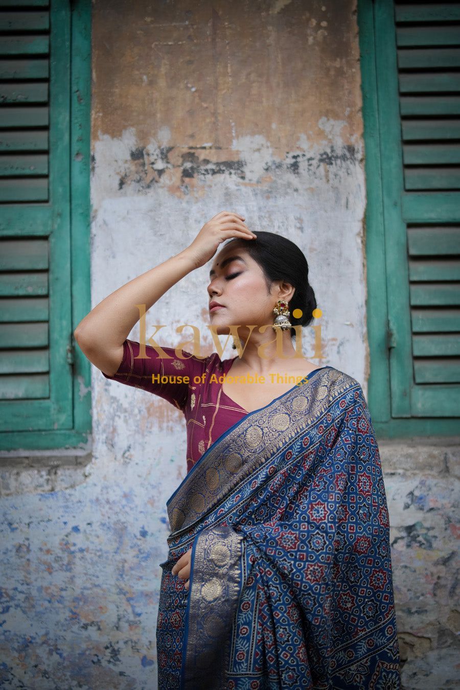 Woman wearing a traditional blue and gold patterned ajrakh saree standing against a rustic wall