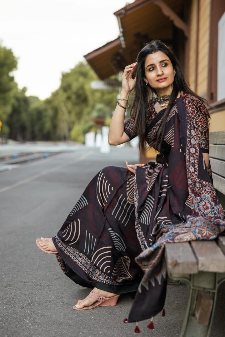 Kawaii ajrakh saree in black with traditional geometric patterns worn by a woman sitting on a bench