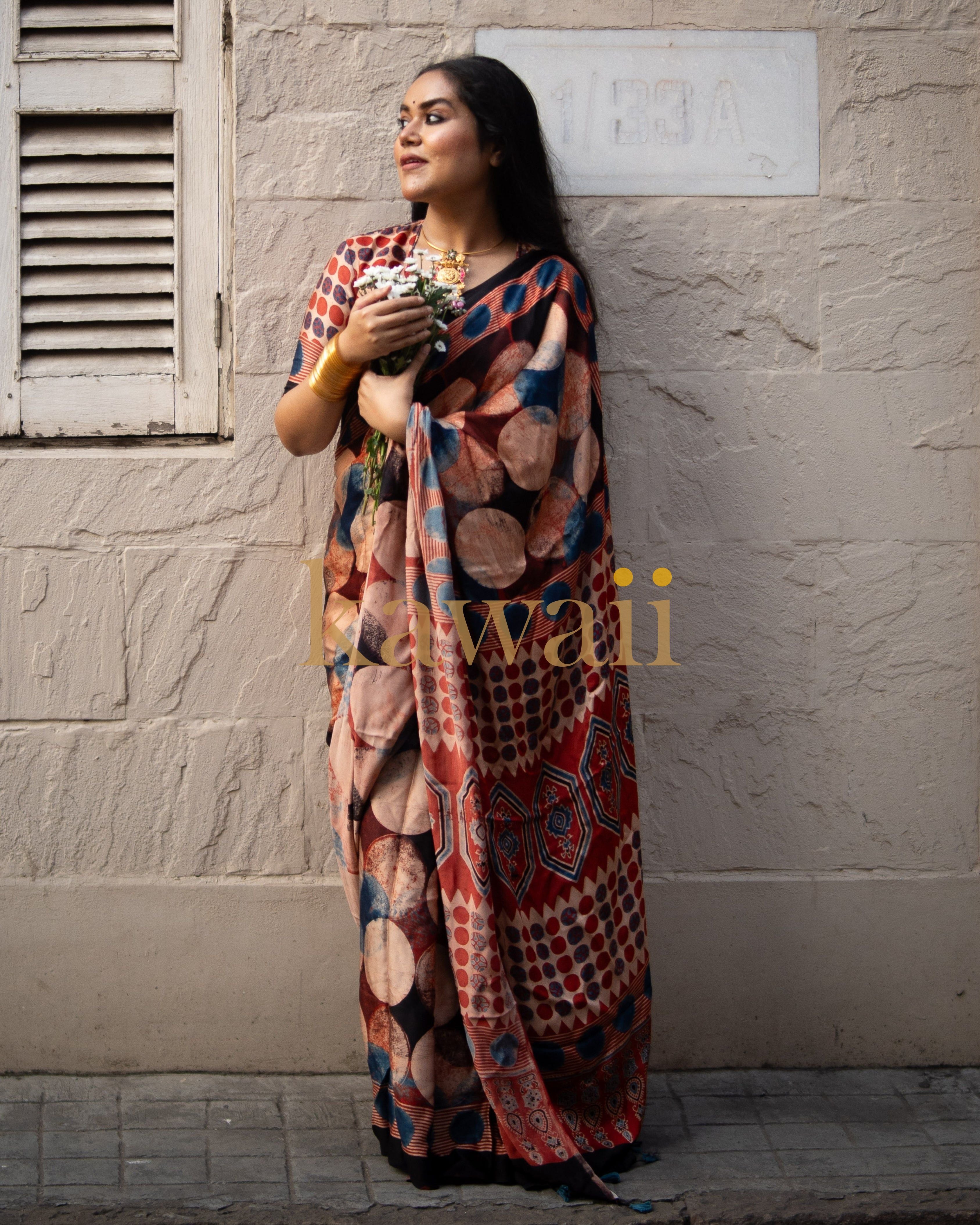 Woman wearing colorful ajrakh saree with geometric and circular patterns standing against textured wall