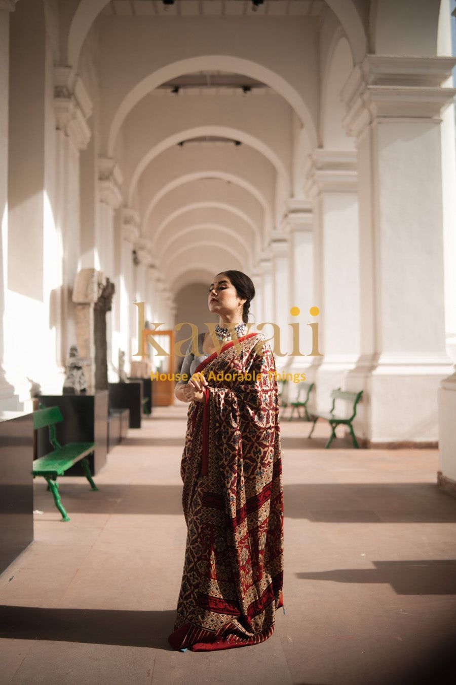 Woman wearing traditional red and black ajrakh saree by Kawaii standing in a white arched corridor