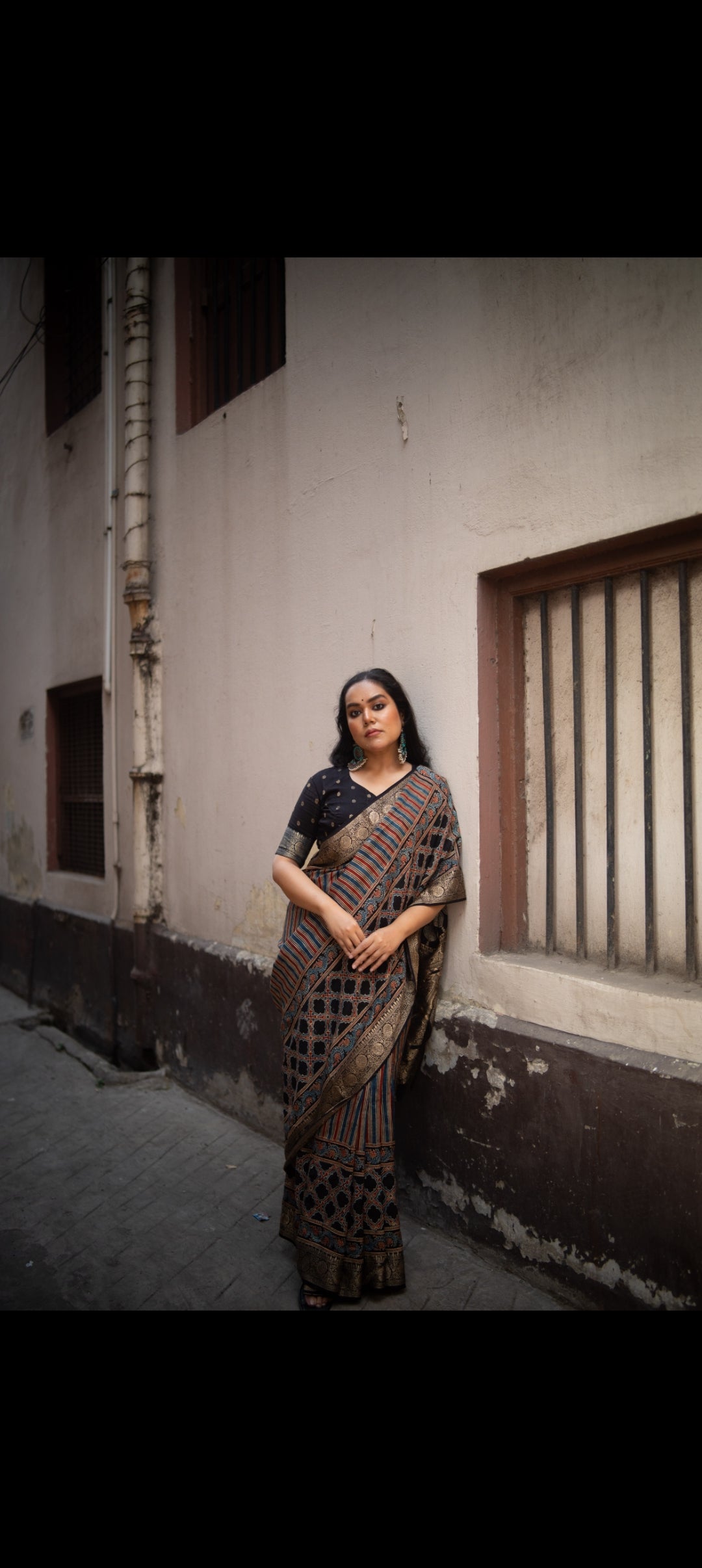 Woman wearing Kawaii ajrakh saree with traditional geometric patterns standing against a rustic wall