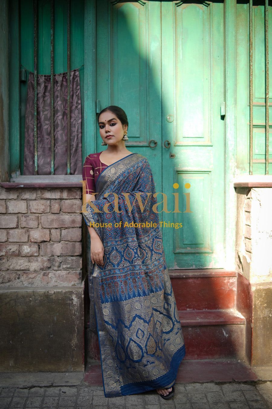 Woman wearing blue and gold ajrakh saree standing by a rustic green door in natural light