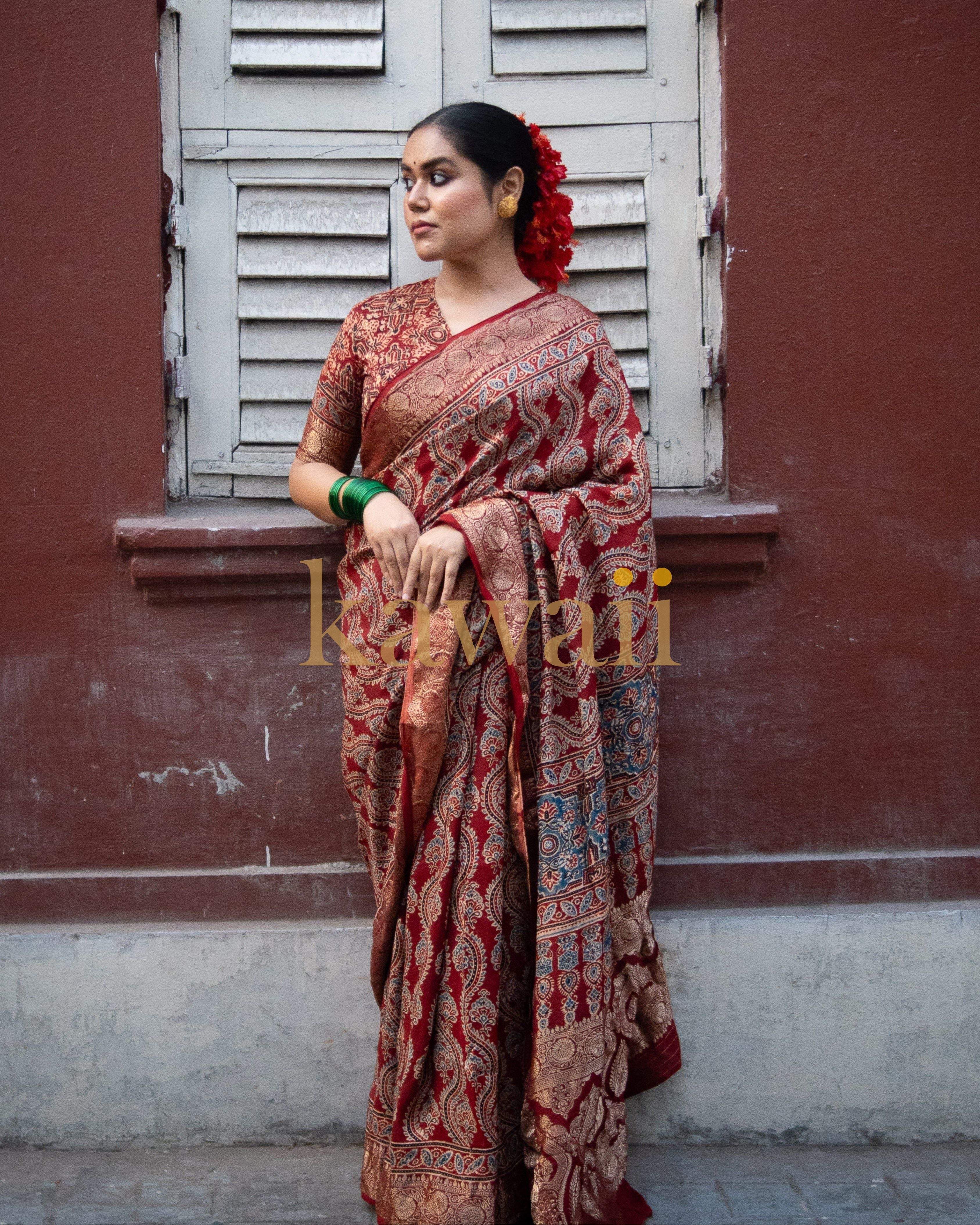 Woman wearing a traditional red and brown printed ajrakh saree by Kawaii standing against a rustic wall