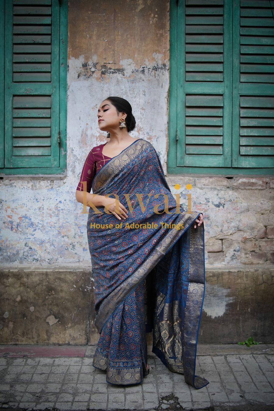 Woman wearing a traditional blue and gold patterned ajrakh saree by Kawaii standing against a rustic wall