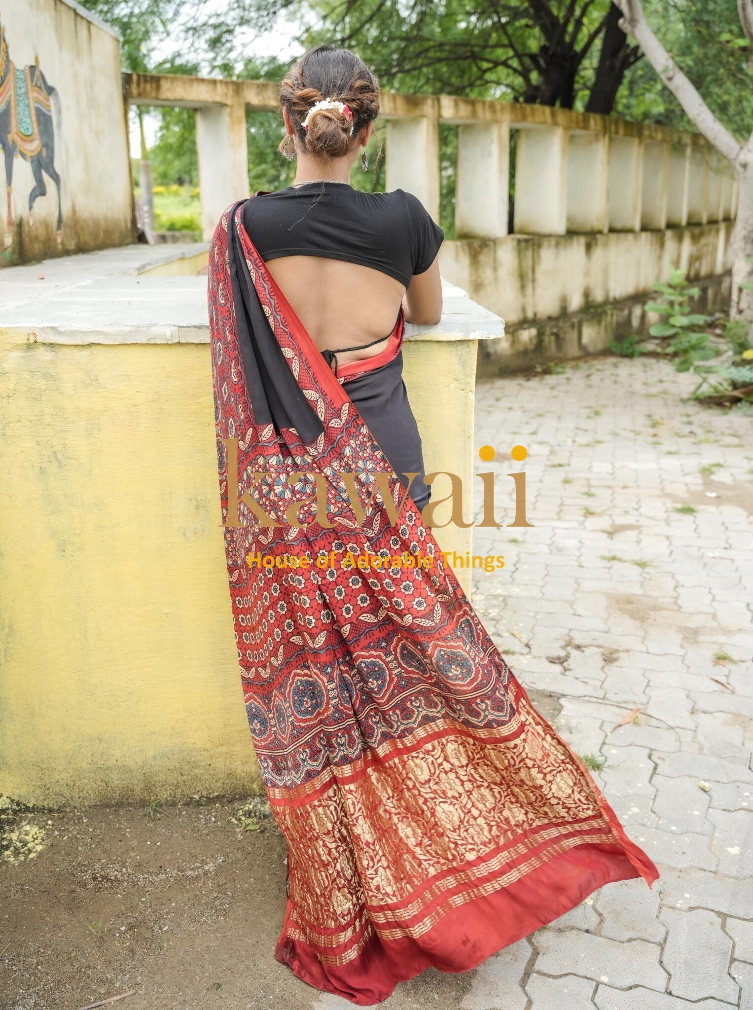 Woman wearing a traditional red and black ajrakh saree by Kawaii with intricate patterns and gold detailing