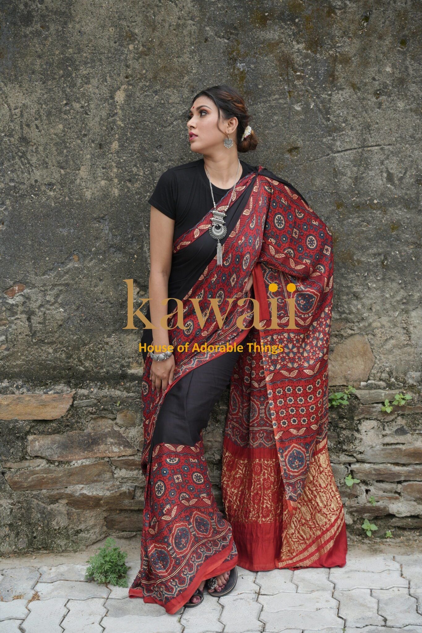 Woman wearing a red and black ajrakh saree with traditional patterns by Kawaii against a stone wall