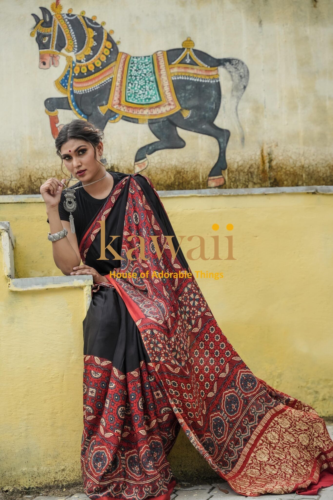 Woman wearing a red and black ajrakh saree by Kawaii with traditional patterns sitting against a yellow wall