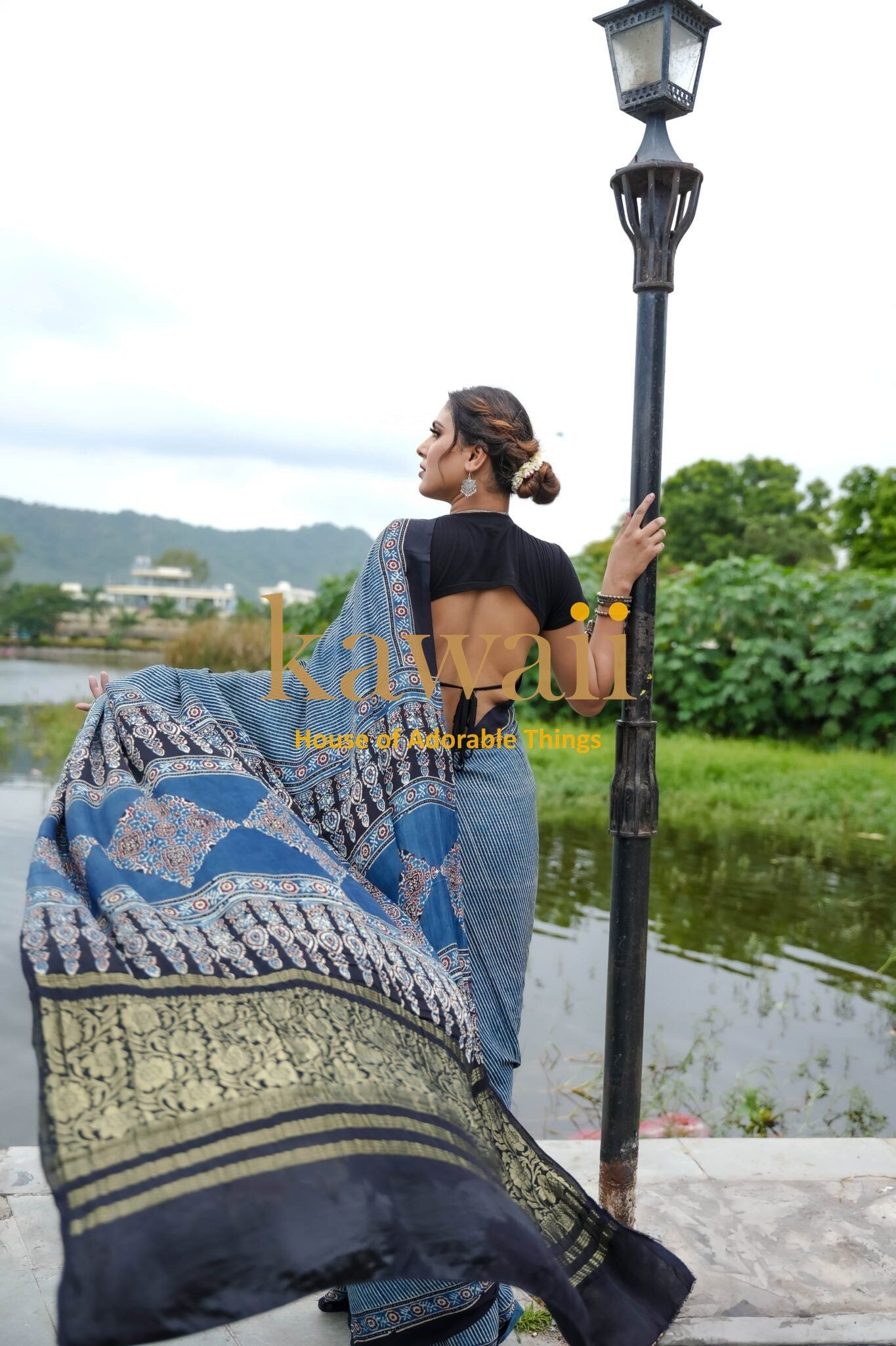 Woman wearing blue and black Ajrakh saree by Kawaii standing near water with landscape background ajrakh sarees online