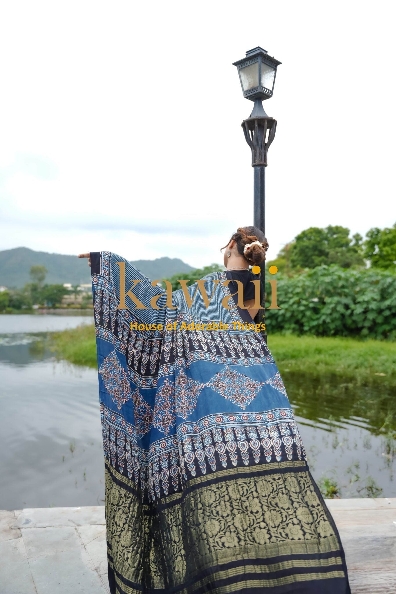 Woman wearing blue and black Ajrakh saree outdoors by the lake showcasing ajrakh sarees online