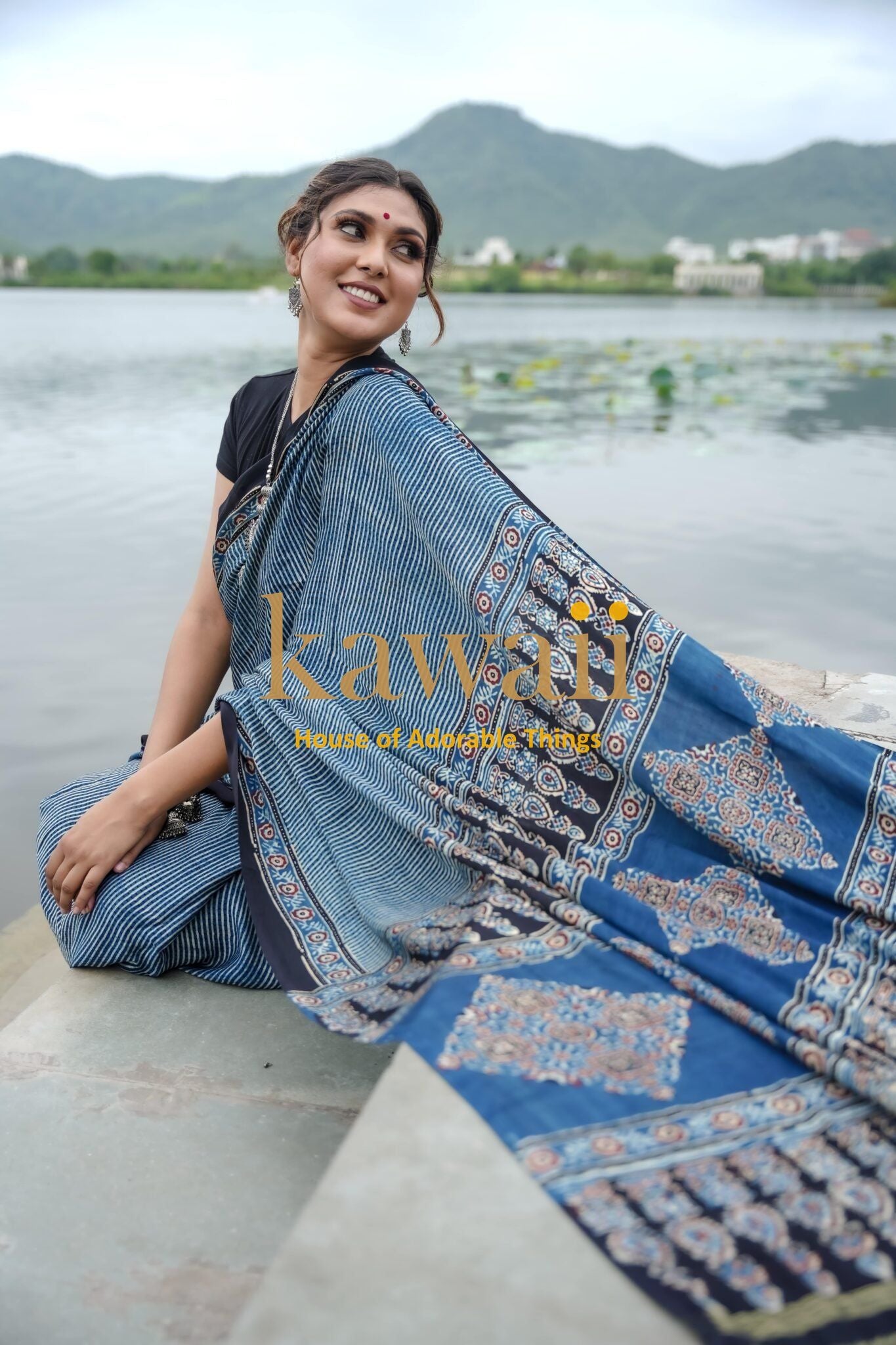 Woman wearing Kawaii ajrakh saree sitting by the lake showcasing blue ajrakh sarees online