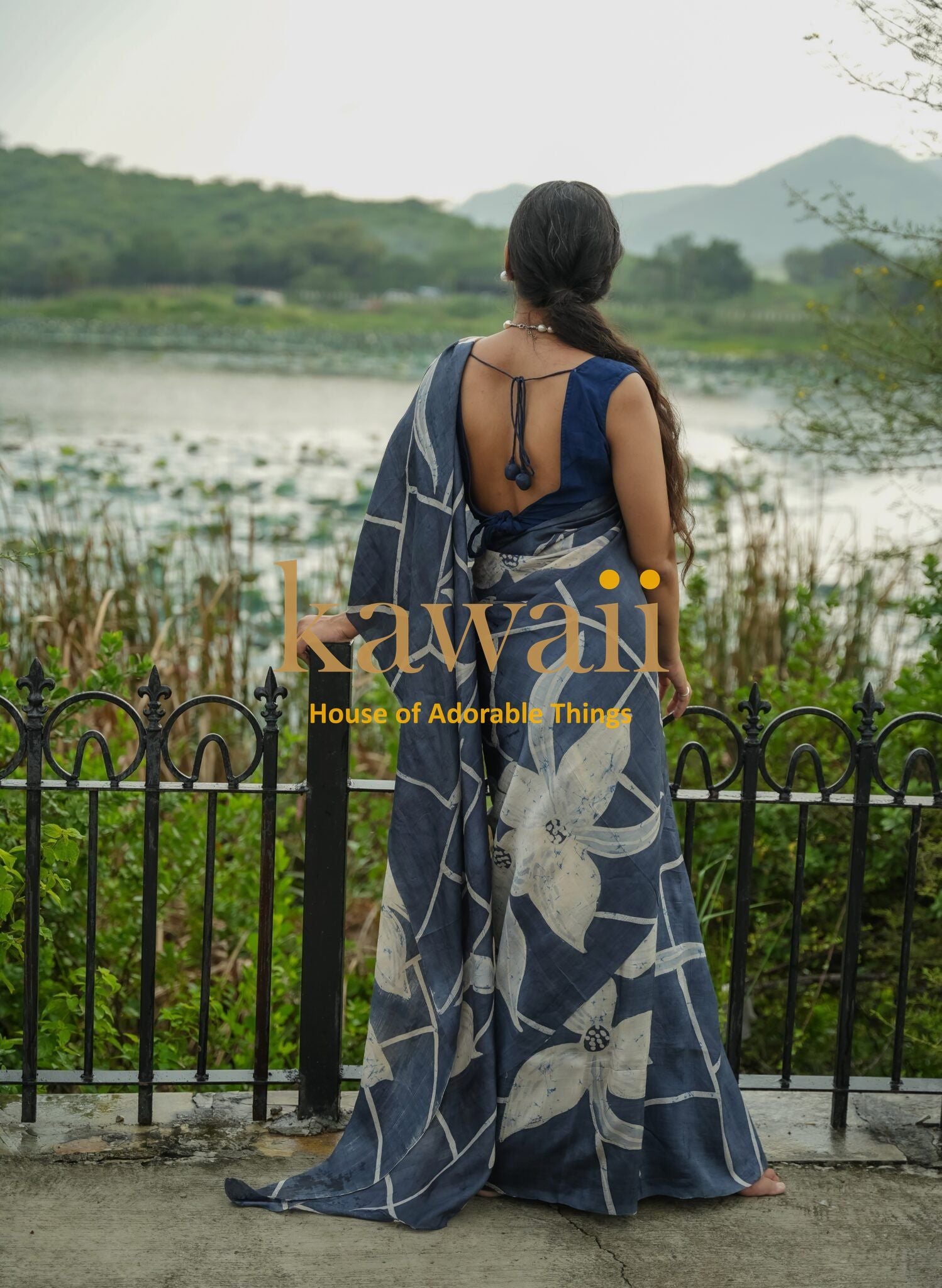 Woman wearing a blue and white floral batik saree by Kawaii standing near a lake with hills in the background