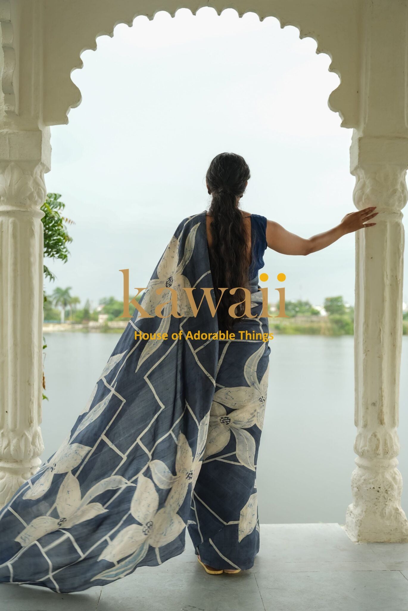 Woman wearing a navy blue and white floral batik saree standing under an arched balcony overlooking water