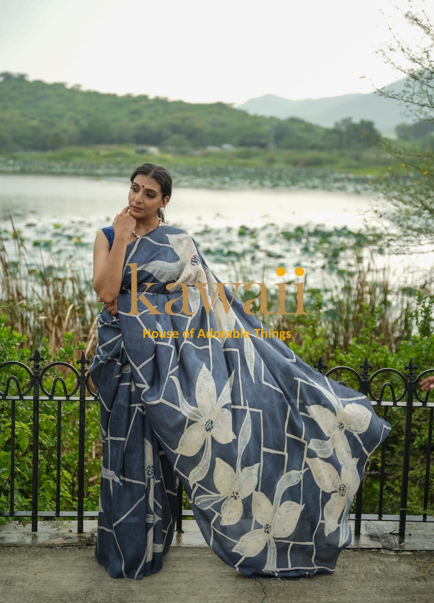 Woman wearing a blue and white batik saree with large floral patterns standing near a lake