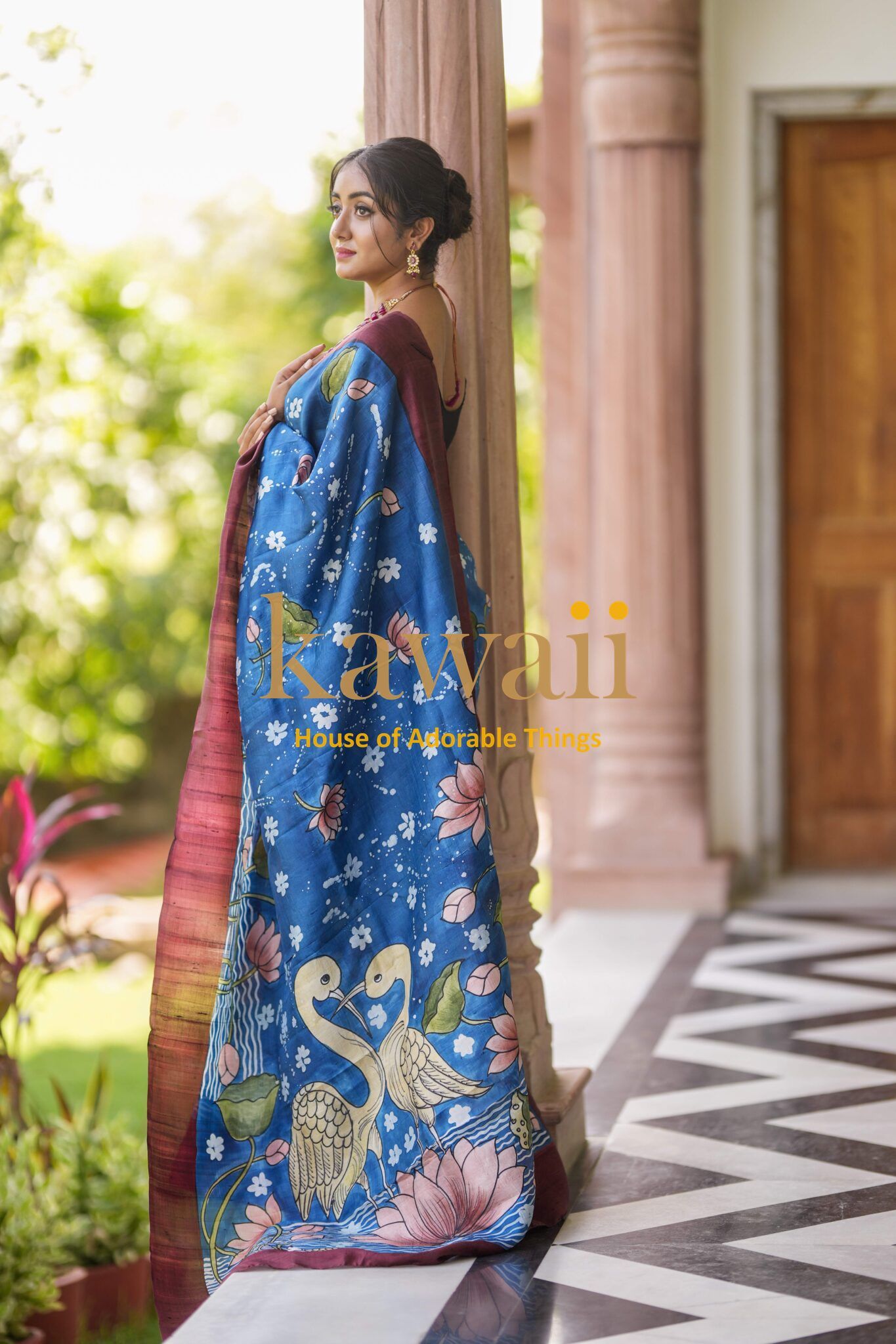 Kawaii Kalamkari saree in blue with intricate batik saree patterns worn by a woman standing on a veranda