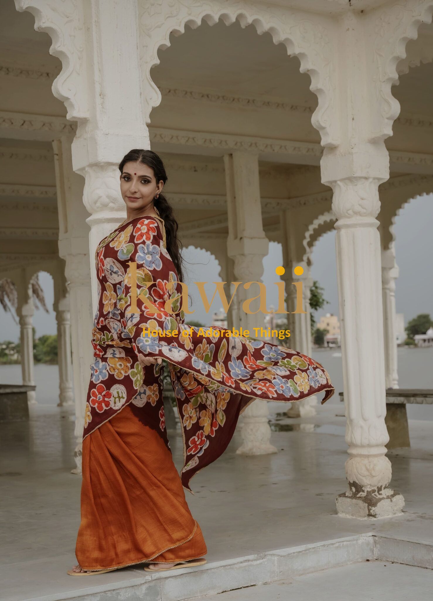 Kawaii batik saree with vibrant floral patterns and orange pleated drape worn by model in traditional setting