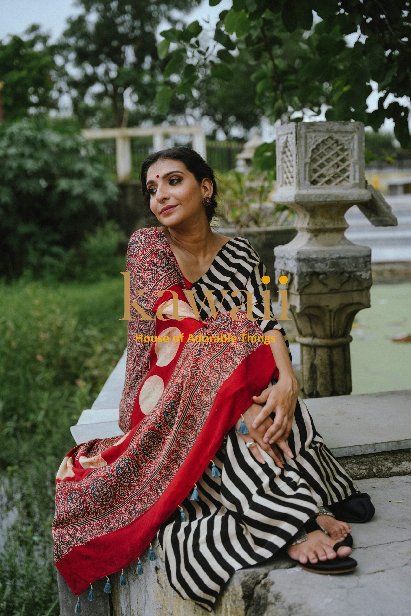 Woman wearing Best Handcrafted Authentic Ajrakh Saree Online with black and white stripes and red patterned border sitting outdoors