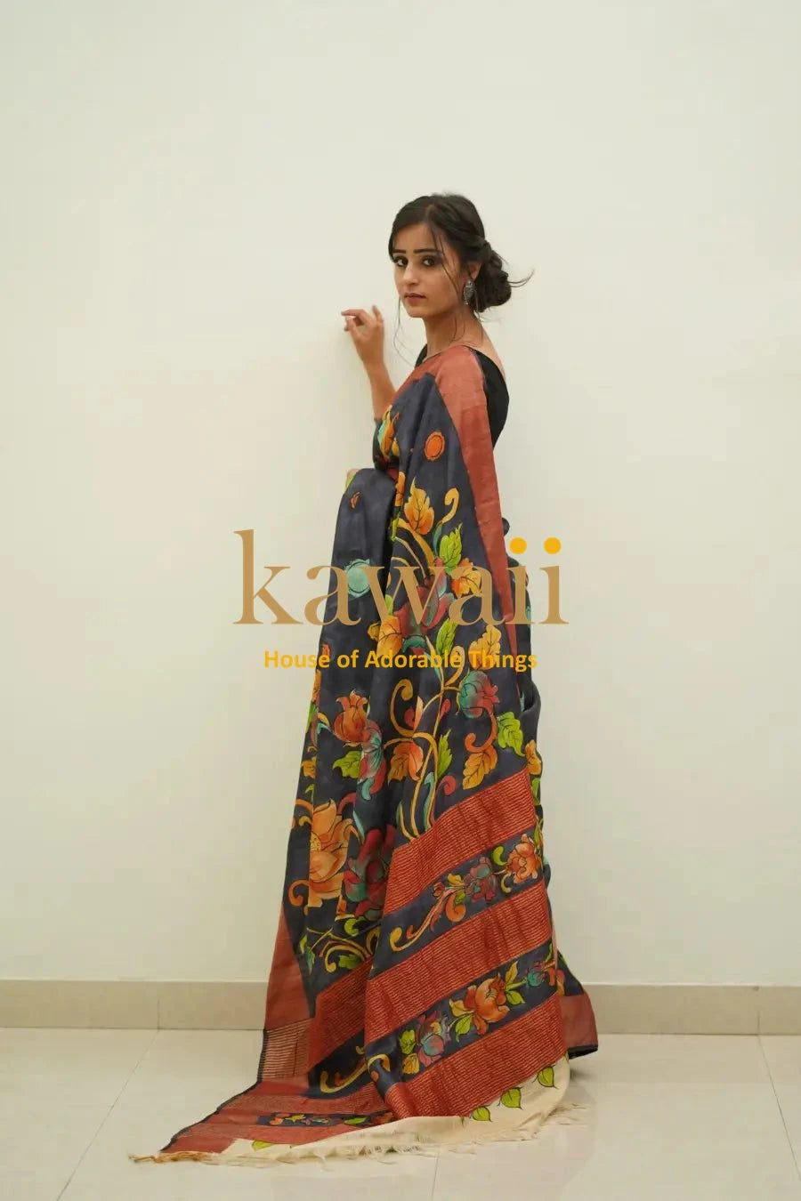 Woman wearing a colorful kalamkari saree with floral and traditional patterns standing against a plain wall