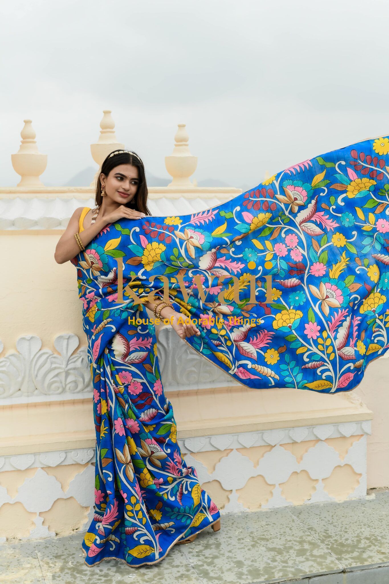 Woman wearing vibrant blue kalamkari saree with colorful floral patterns by Kawaii