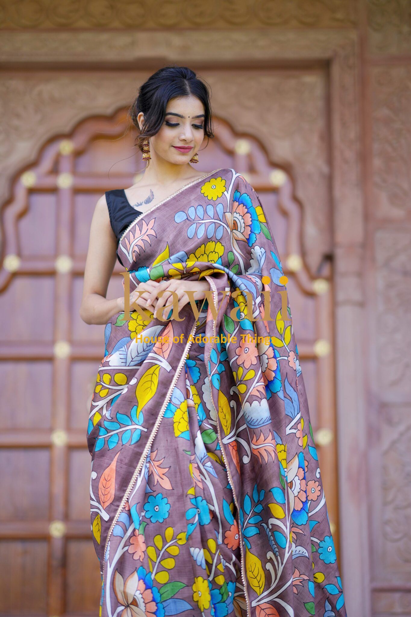 Kawaii kalamkari saree with vibrant floral patterns draped on a woman in front of a traditional wooden door